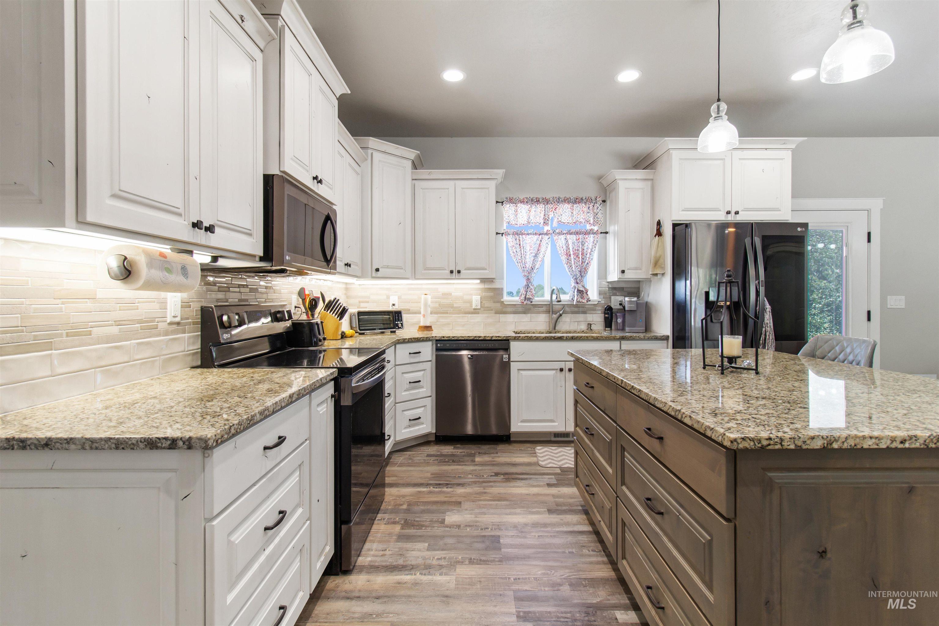 Kitchen with stainless steel appliances, light stone countertops, white cabinetry, pendant lighting, and decorative backsplash