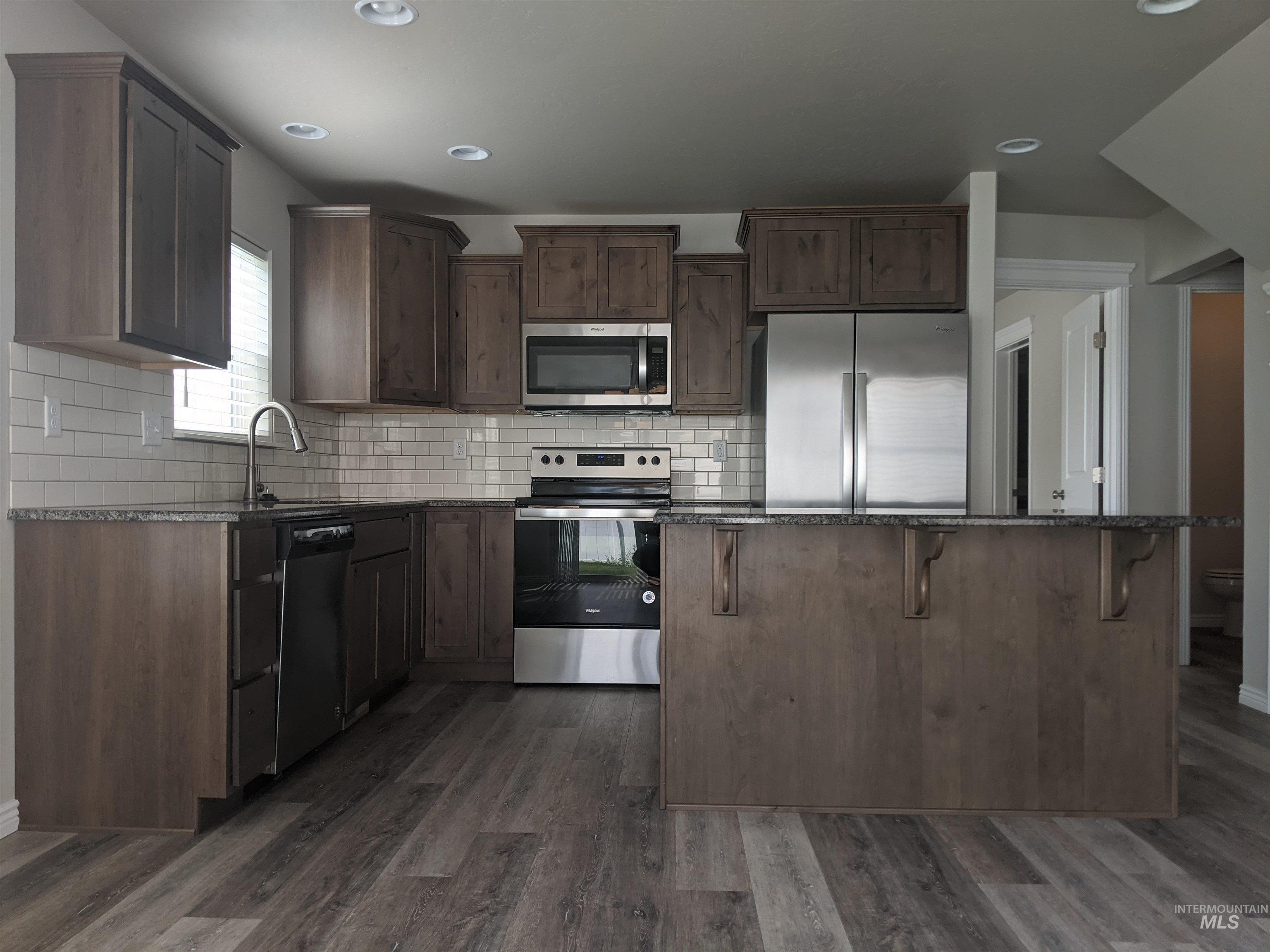 Kitchen with dark stone counters, stainless steel appliances, dark brown cabinetry, dark wood-style floors, and tasteful backsplash