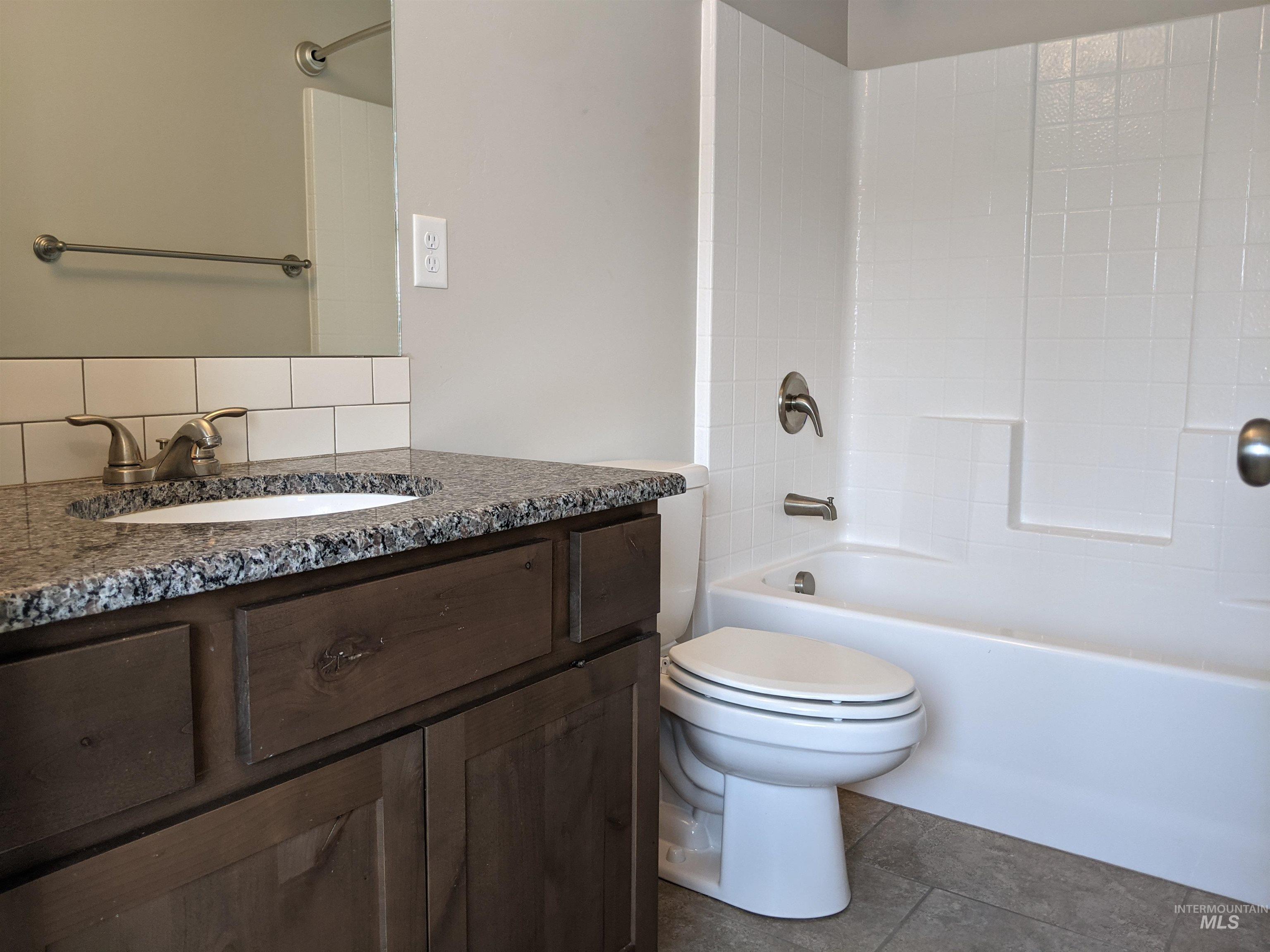 Full bath with vanity, tub / shower combination, decorative backsplash, and dark tile patterned floors