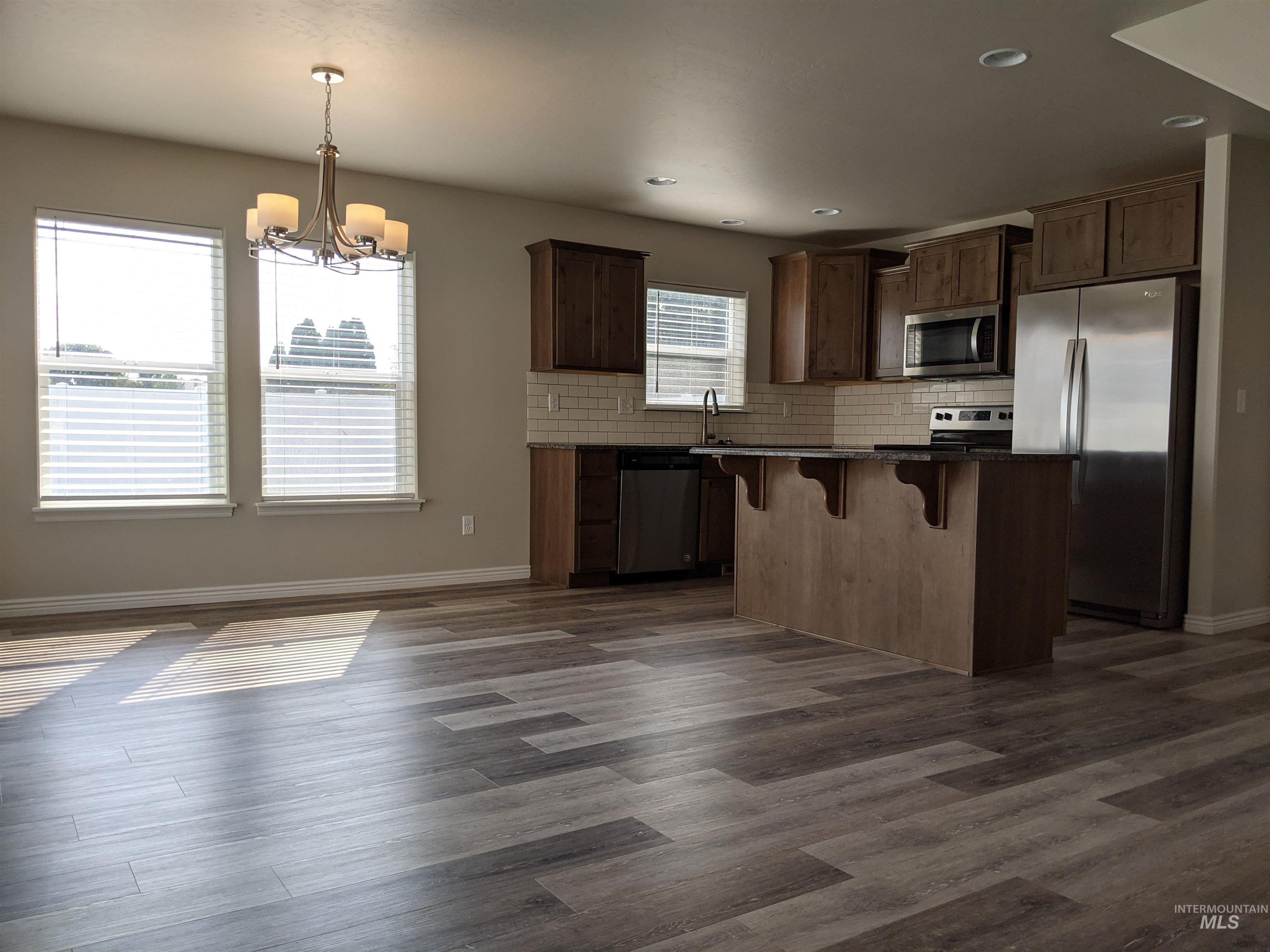 Kitchen featuring stainless steel appliances, a kitchen breakfast bar, decorative backsplash, dark wood-style floors, and pendant lighting