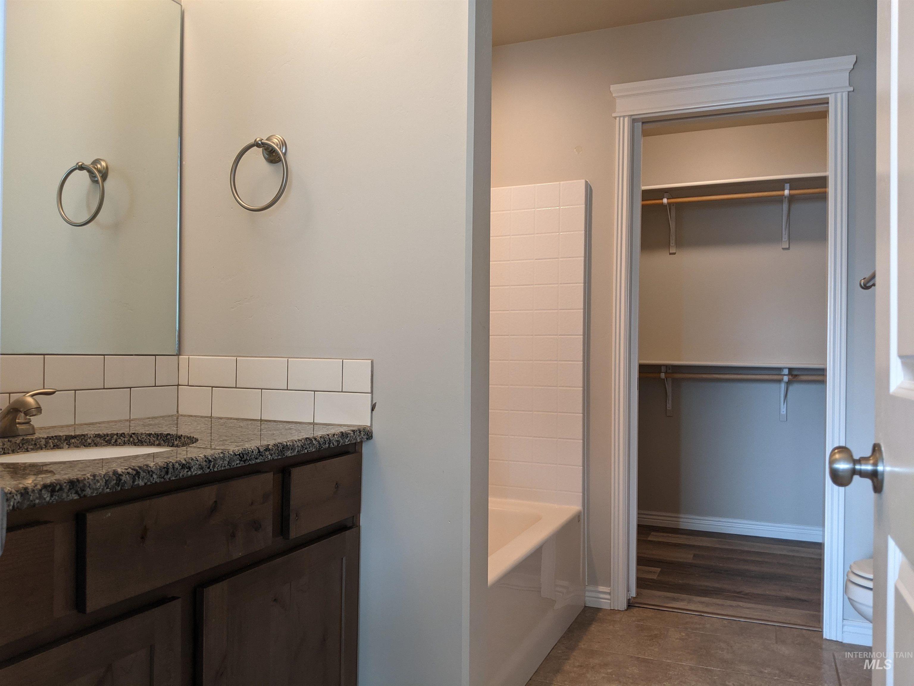 Bathroom with vanity, dark tile patterned flooring, bathtub / shower combination, and a spacious closet