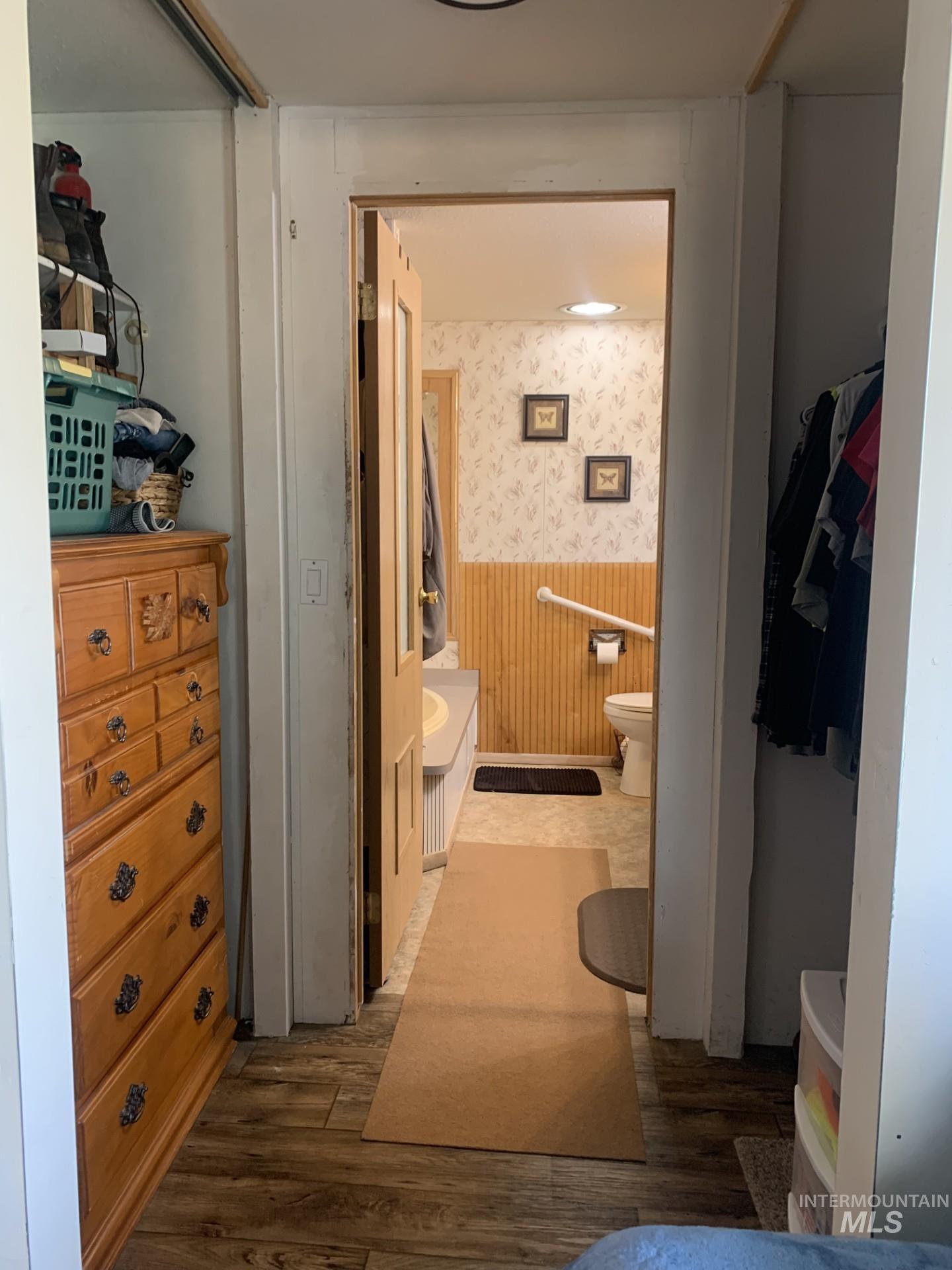 Bathroom featuring wallpapered walls, wainscoting, vanity, dark wood finished floors, and a closet