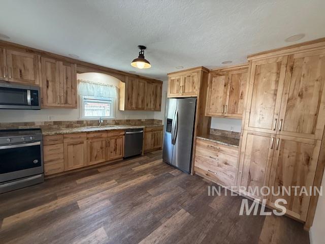Kitchen with appliances with stainless steel finishes, light brown cabinets, dark wood-type flooring, a textured ceiling, and light stone counters