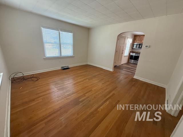 Spare room with arched walkways and wood finished floors