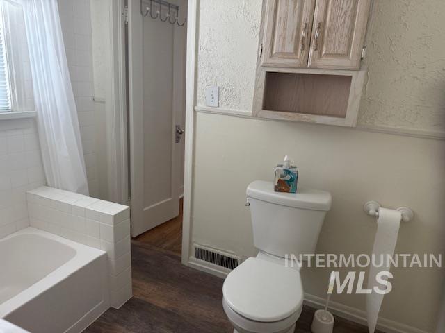 Full bath with dark wood-type flooring, shower / tub combo, and a textured wall
