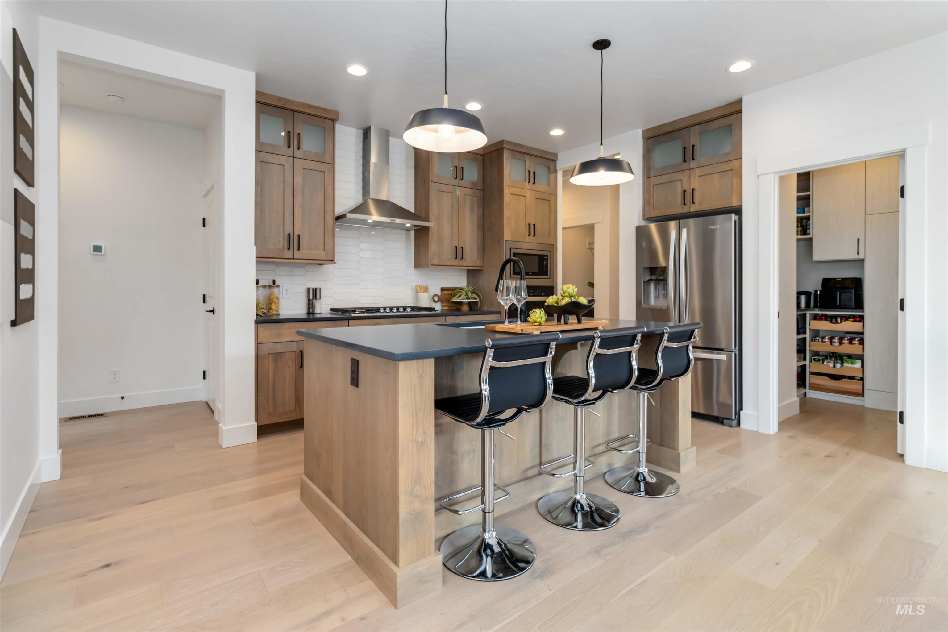 Kitchen featuring tasteful backsplash, stainless steel appliances, a breakfast bar area, a center island with sink, and wall chimney exhaust hood