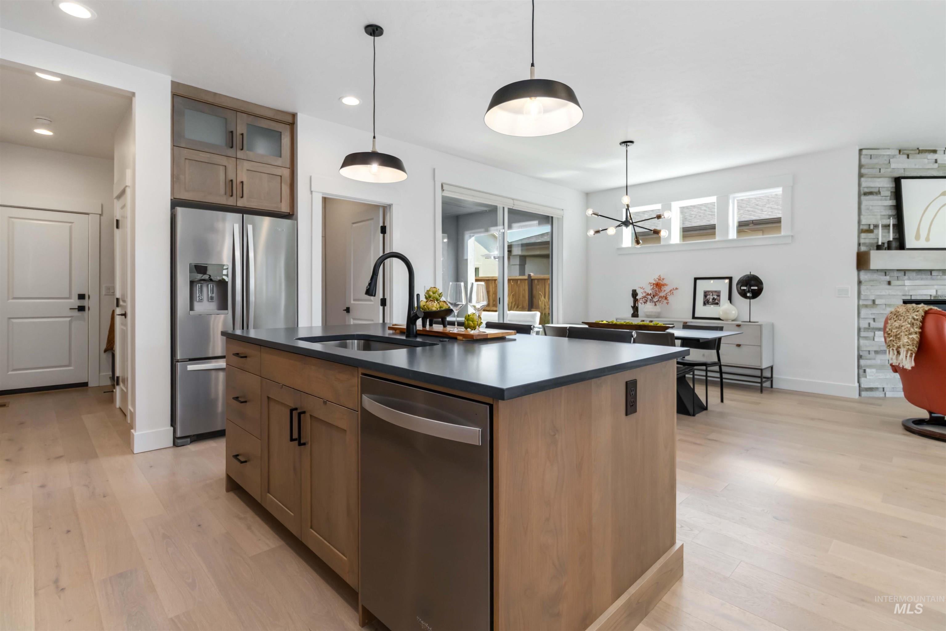 Kitchen with stainless steel appliances, a kitchen island with sink, decorative light fixtures, light wood finished floors, and recessed lighting