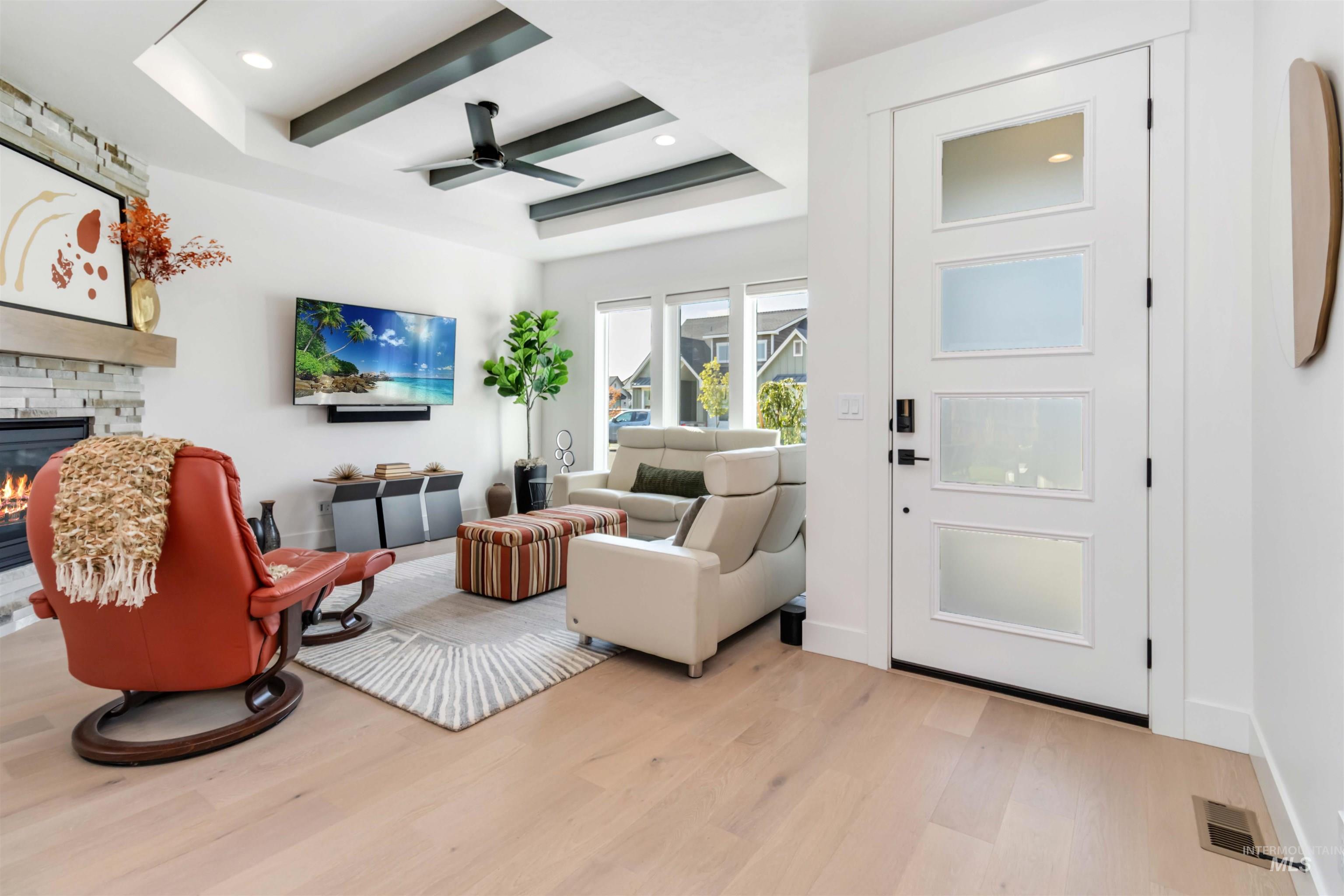 Living area featuring light wood-type flooring, a ceiling fan, a fireplace, recessed lighting, and beamed ceiling