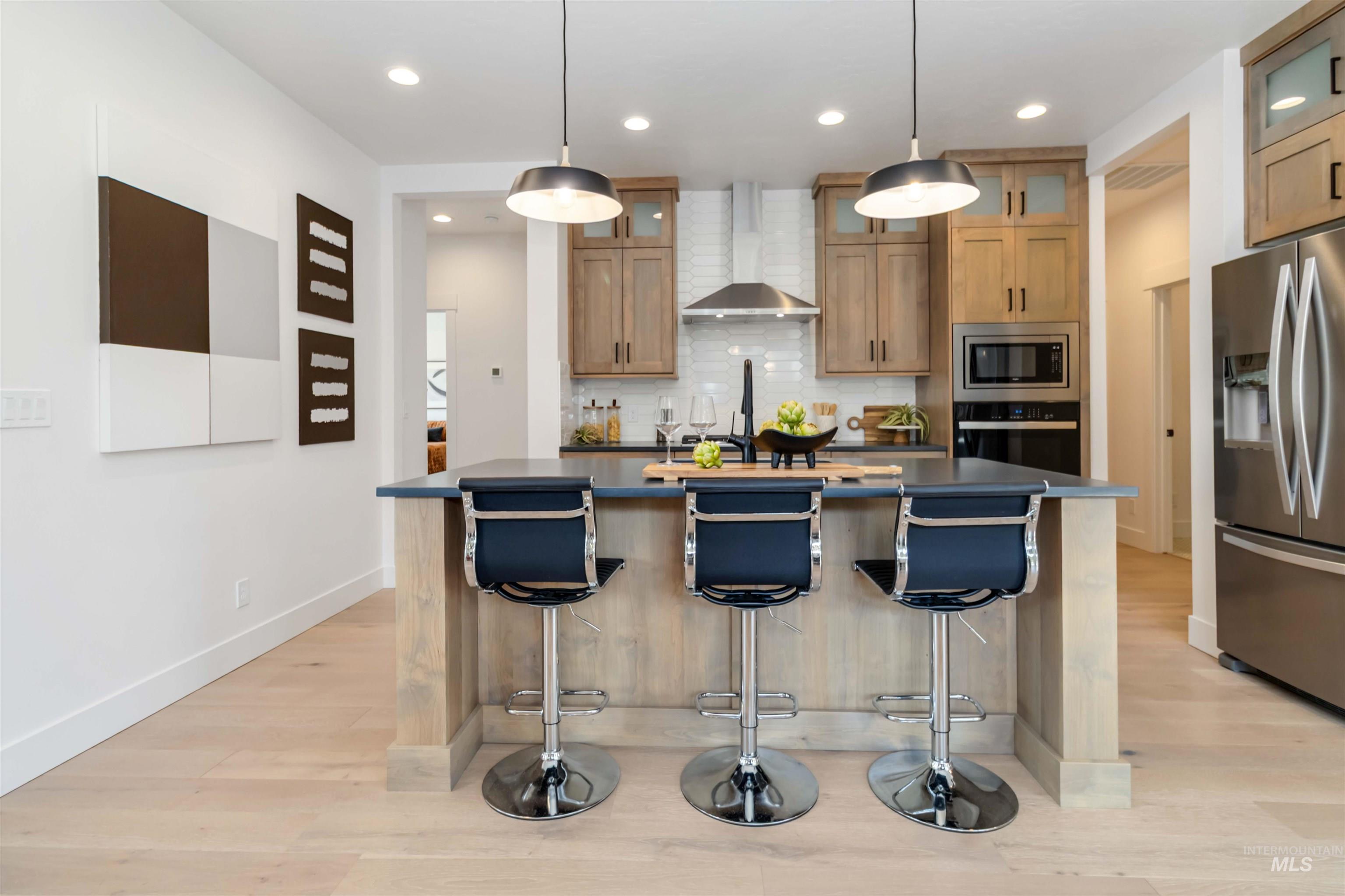Kitchen with decorative backsplash, appliances with stainless steel finishes, pendant lighting, dark countertops, and a center island with sink