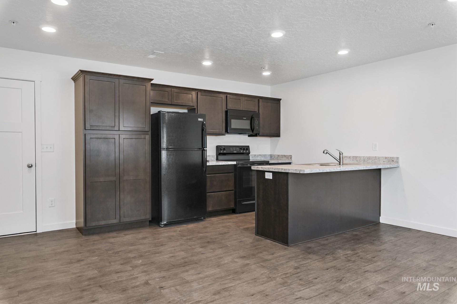 Kitchen featuring dark brown cabinets, black appliances, a peninsula, dark wood-style floors, and a textured ceiling