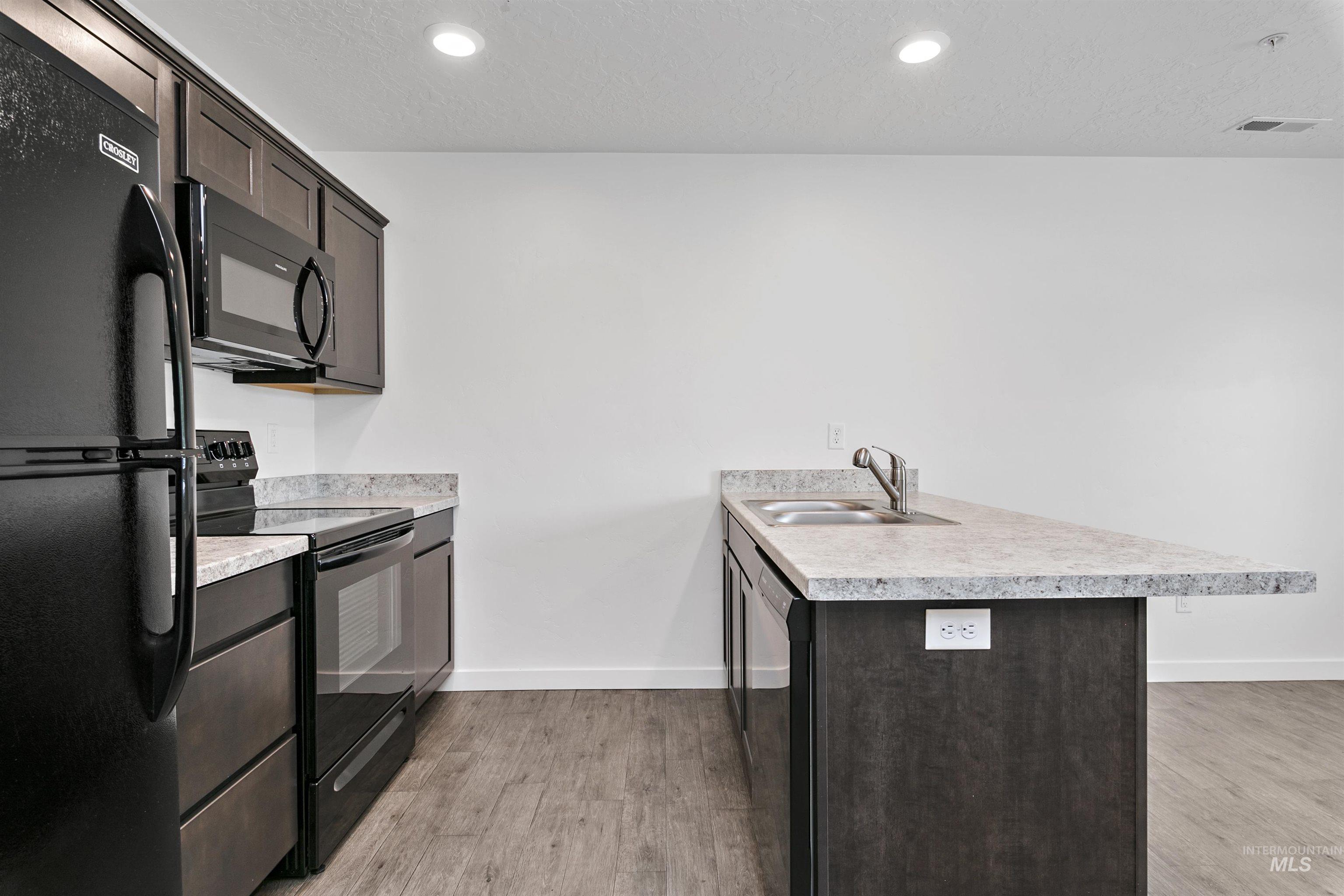 Kitchen featuring a peninsula, black appliances, a textured ceiling, dark brown cabinetry, and light wood finished floors
