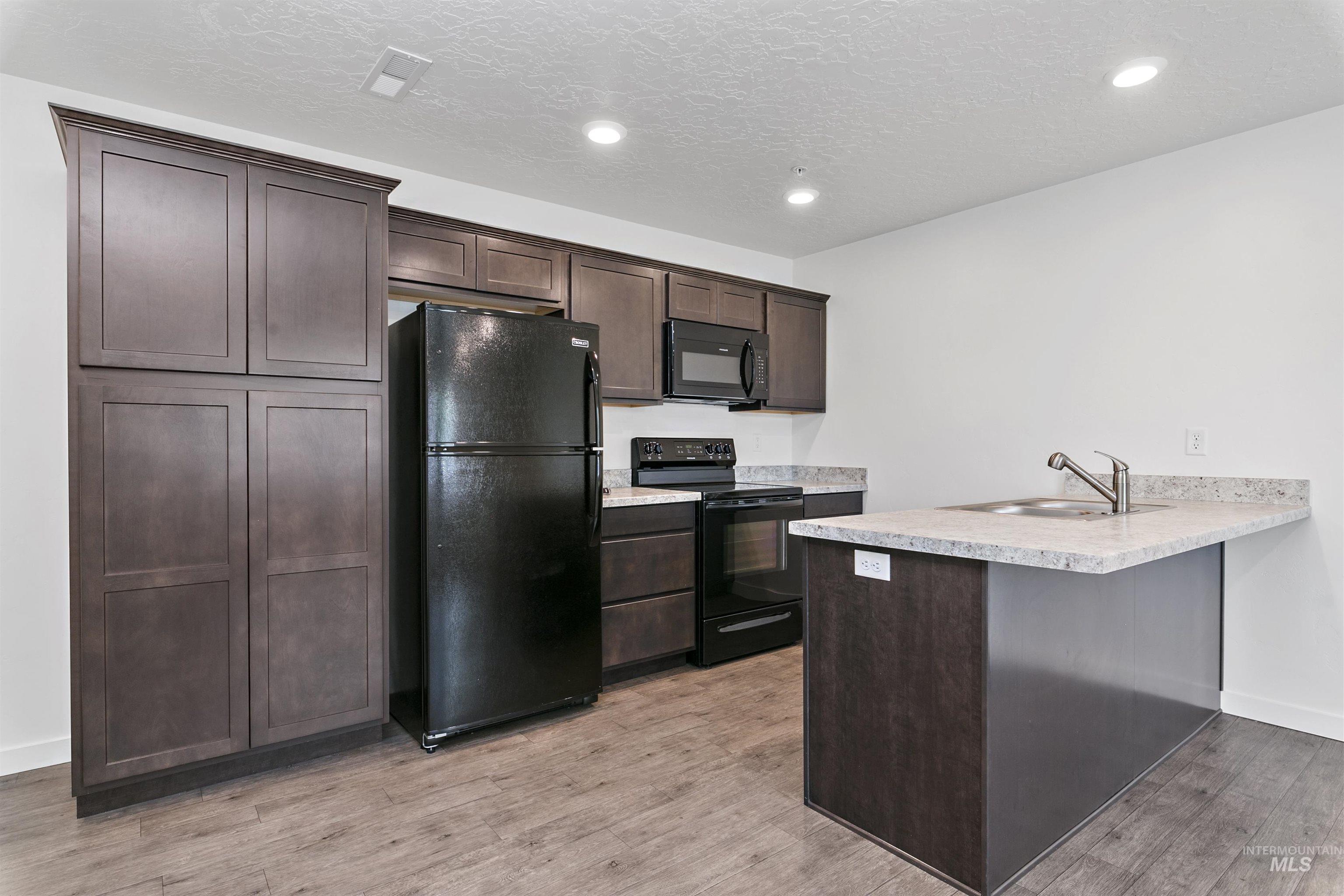 Kitchen with dark brown cabinets, black appliances, light countertops, a peninsula, and light wood finished floors