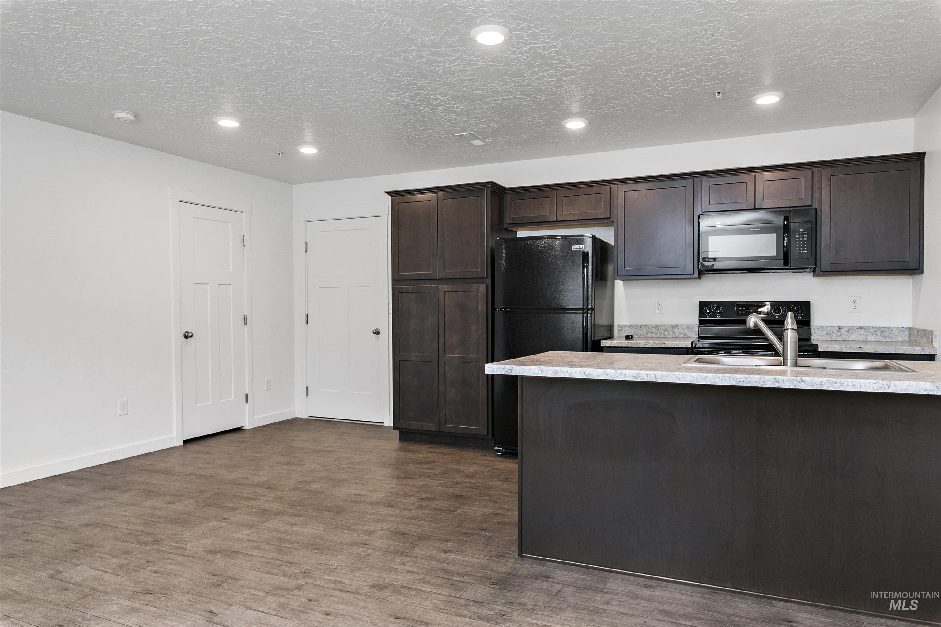Kitchen with dark brown cabinetry, black appliances, dark wood finished floors, recessed lighting, and a textured ceiling
