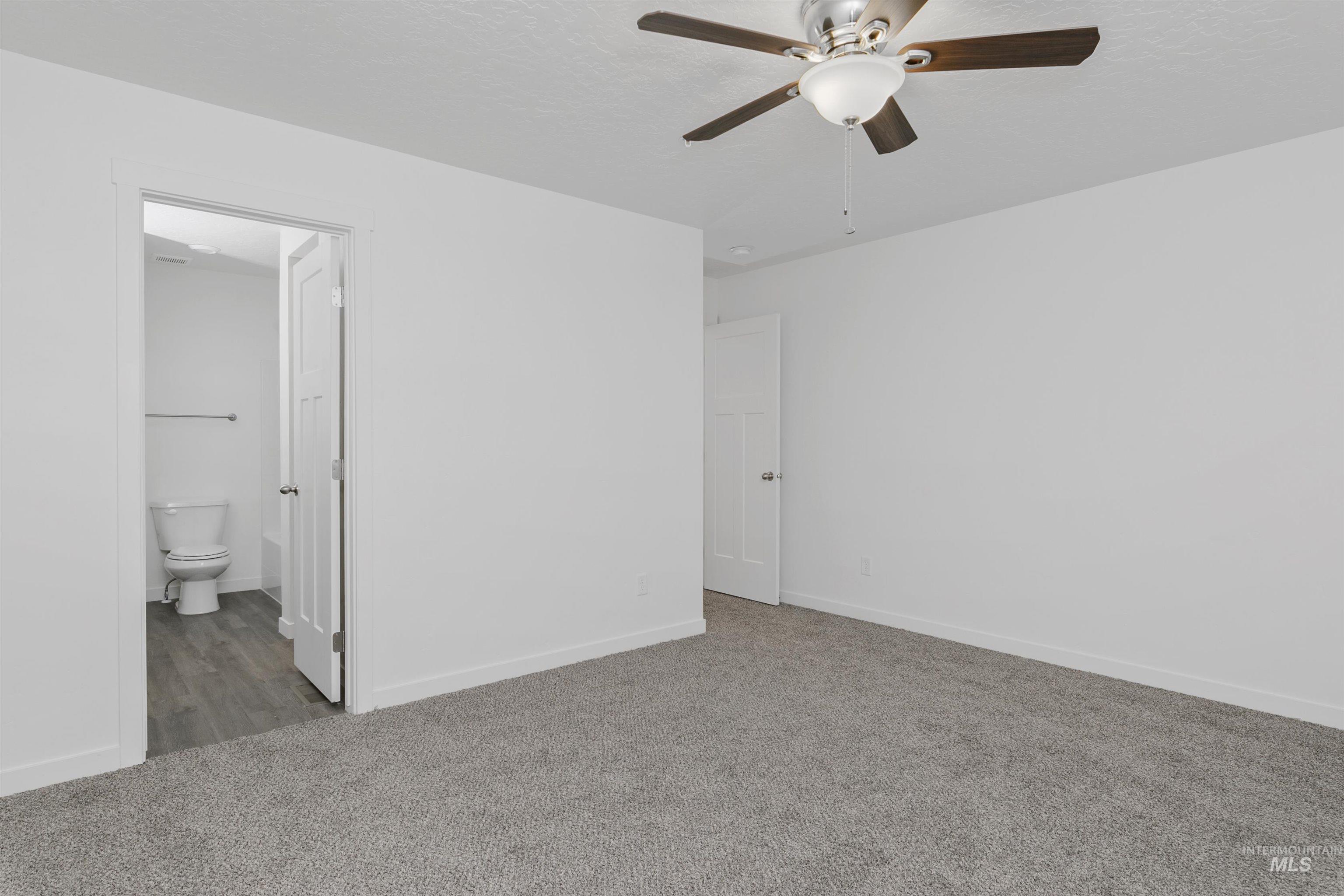 Unfurnished bedroom with carpet flooring, a ceiling fan, ensuite bath, and a textured ceiling