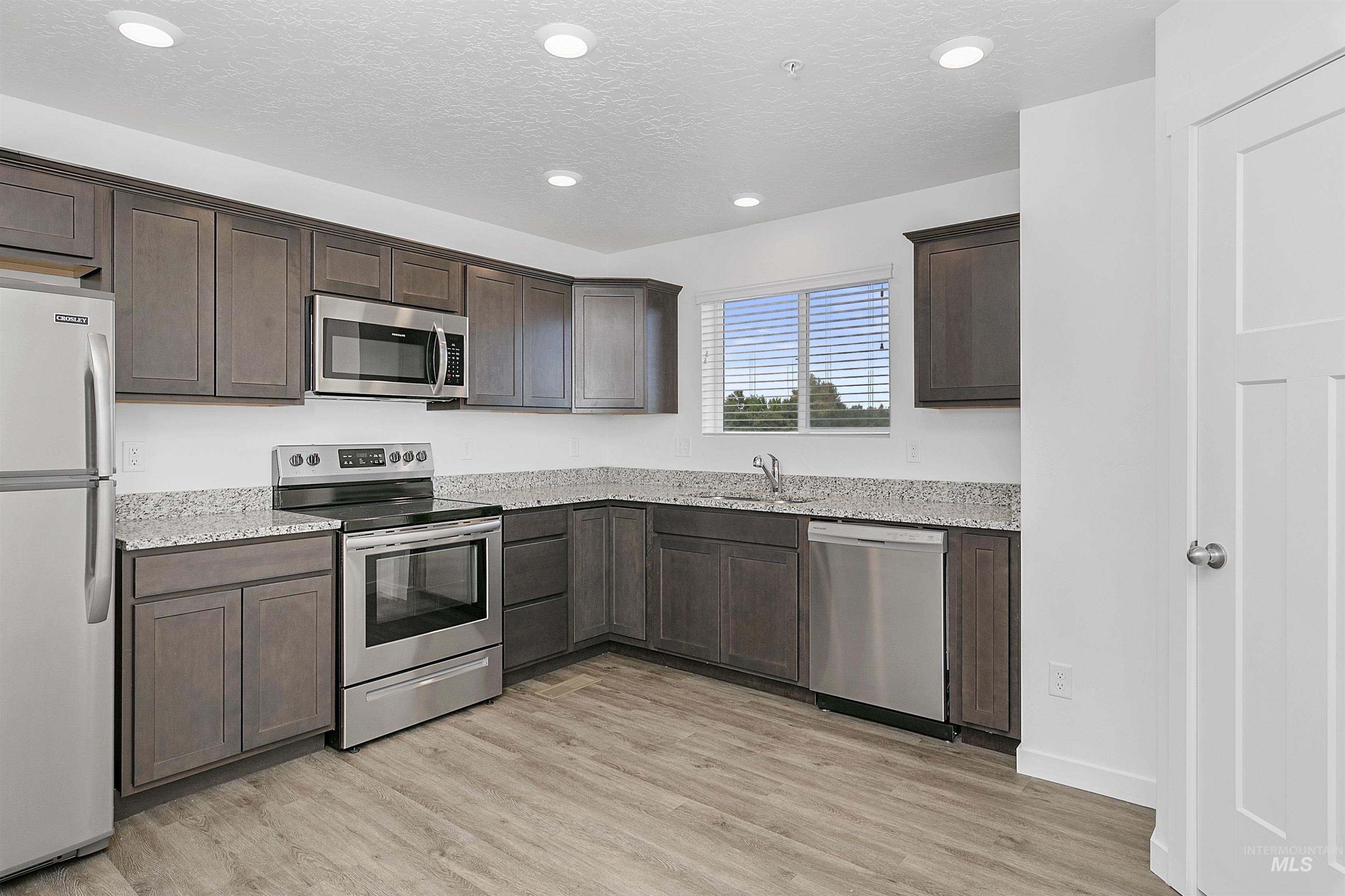 Kitchen featuring stainless steel appliances, light wood finished floors, a textured ceiling, light stone counters, and dark brown cabinets