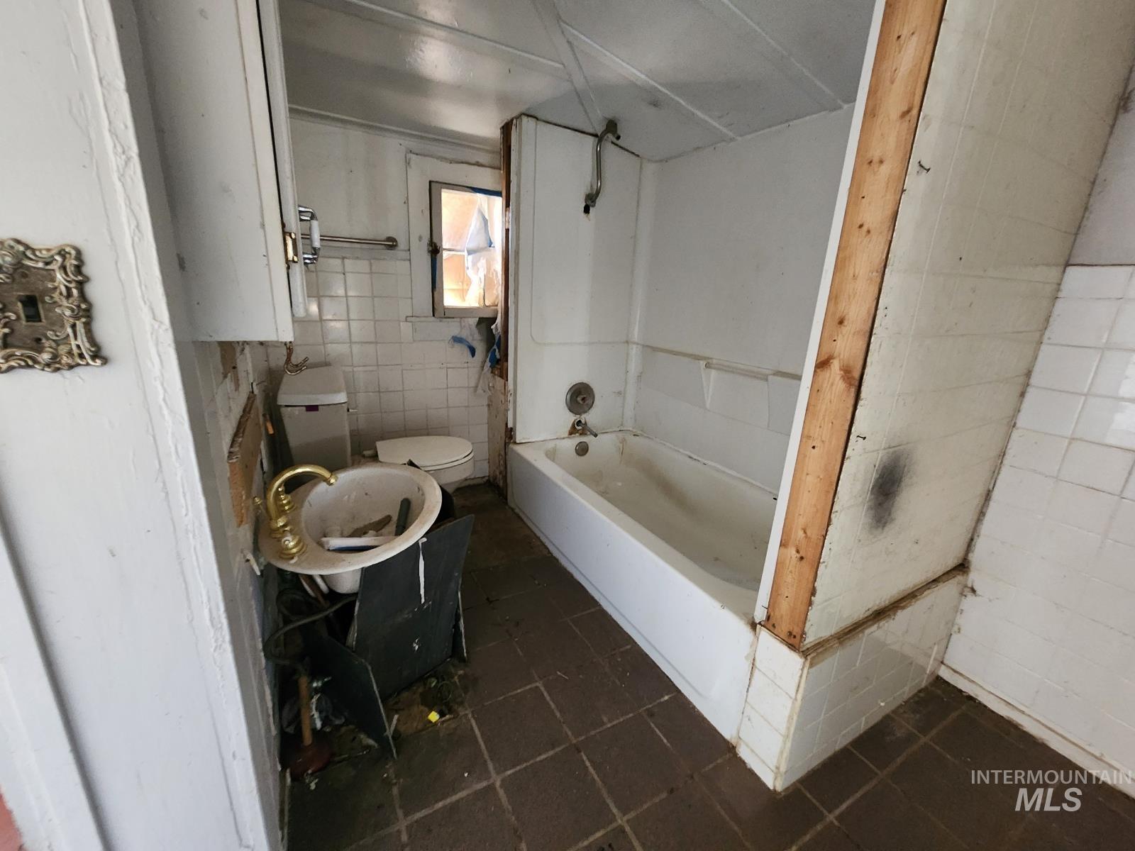 Bathroom with tile walls, dark tile patterned floors, and bathing tub / shower combination