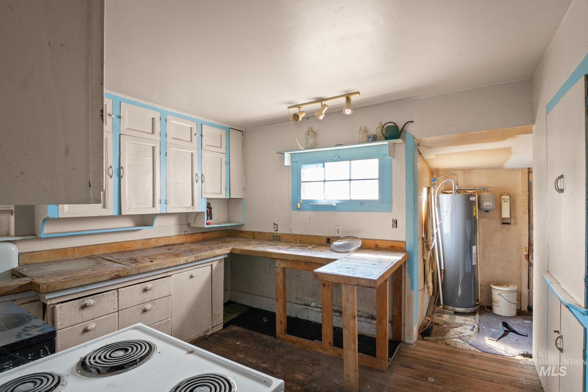 Kitchen with white cabinets, light countertops, electric water heater, dark wood finished floors, and white electric stovetop