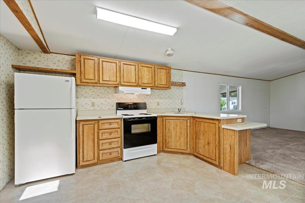 Kitchen featuring a peninsula, white appliances, light countertops, wallpapered walls, and light carpet