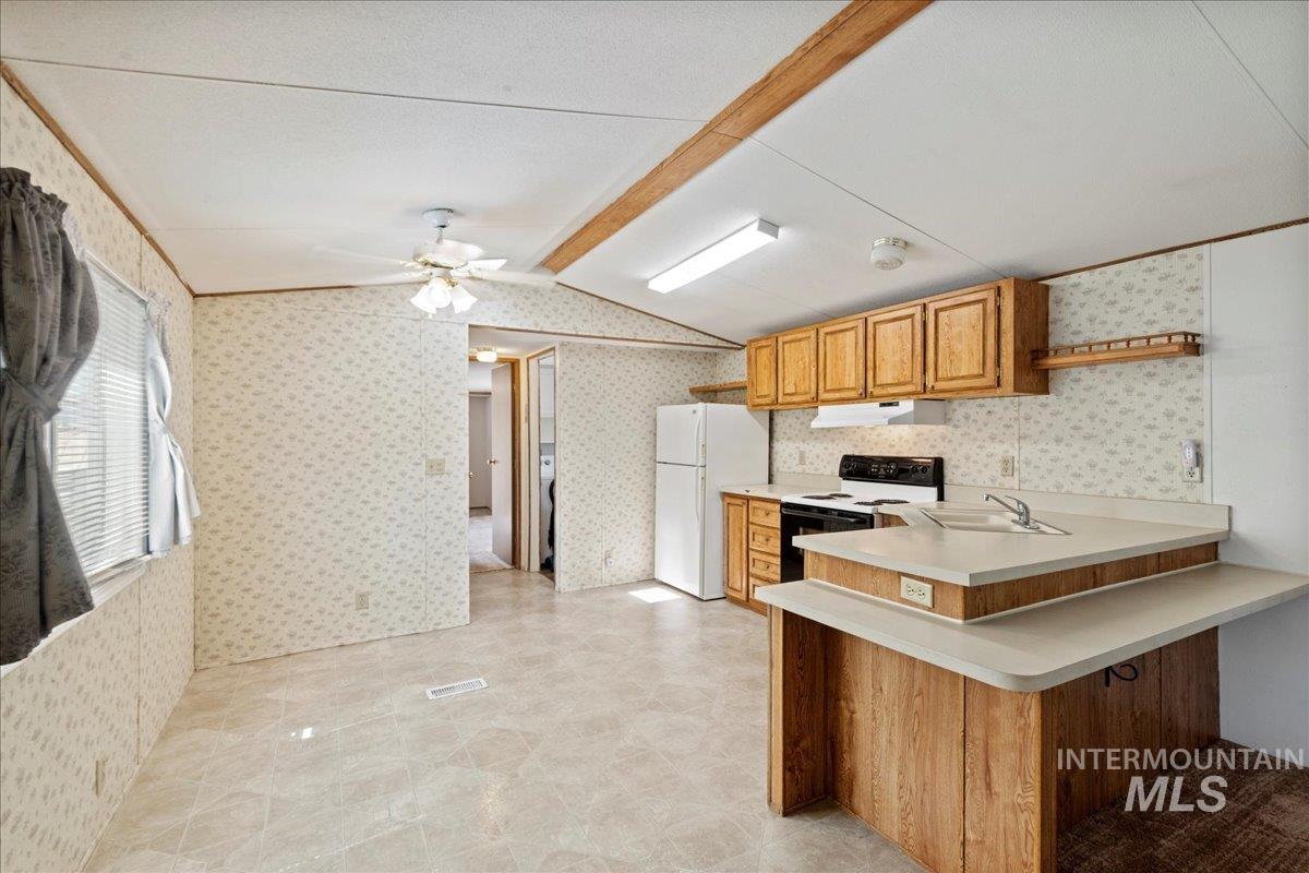 Kitchen featuring light countertops, a peninsula, white appliances, vaulted ceiling, and brown cabinetry