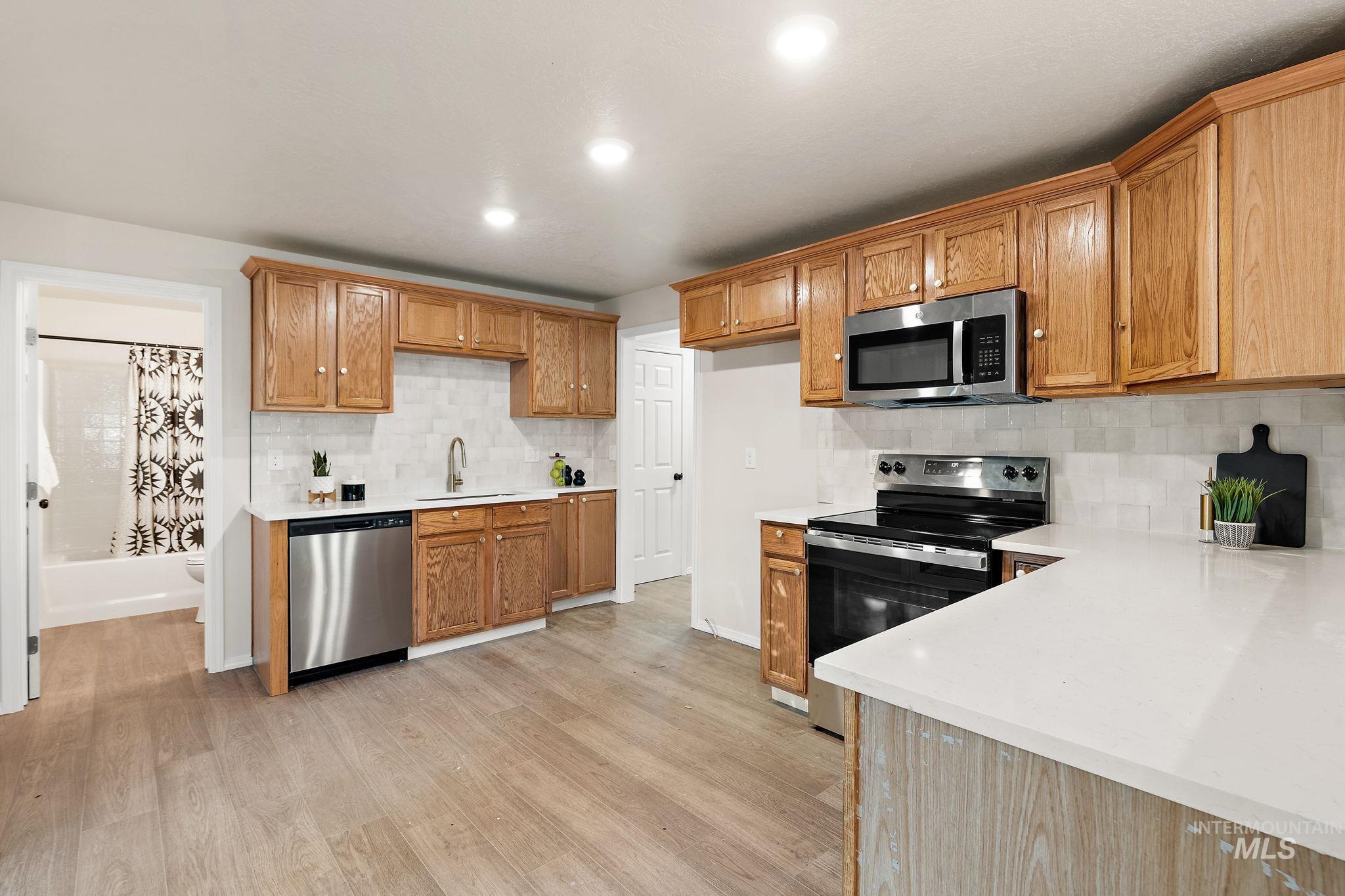 Kitchen featuring stainless steel appliances, decorative backsplash, light wood-style floors, recessed lighting, and brown cabinetry