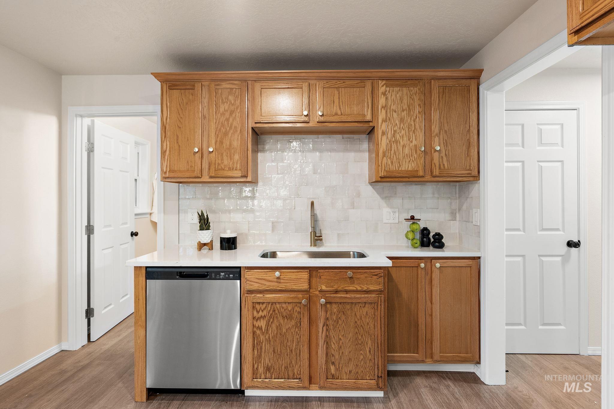 Kitchen featuring brown cabinets, backsplash, dishwasher, and light wood-style flooring