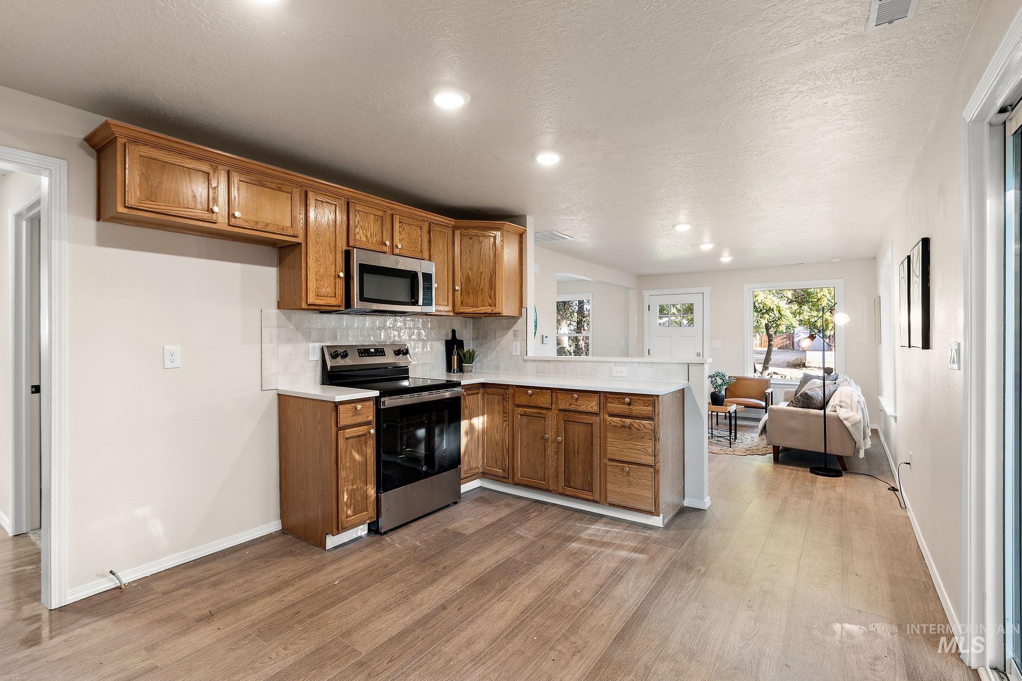 Kitchen featuring brown cabinets, backsplash, stainless steel appliances, open floor plan, and light countertops