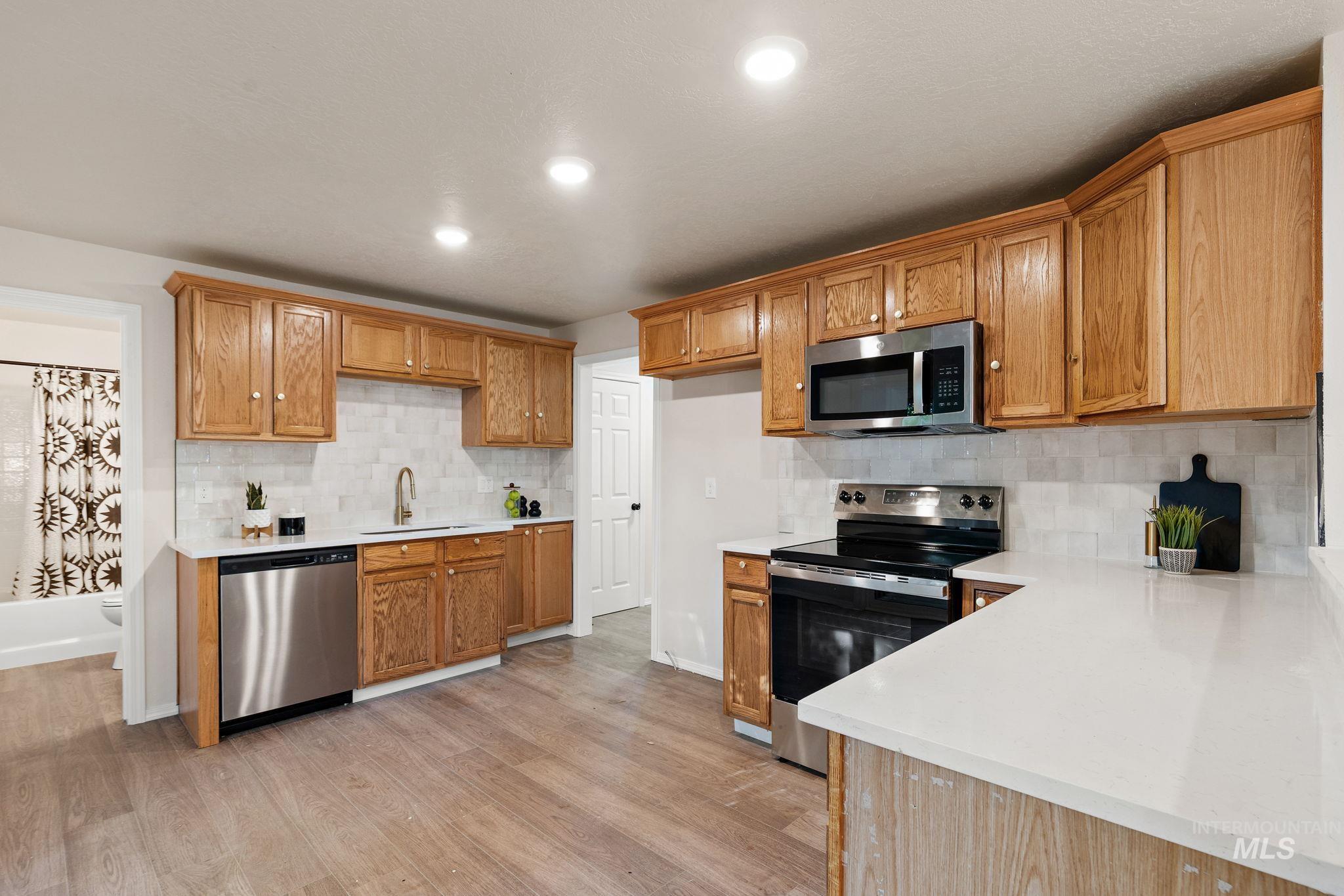 Kitchen with appliances with stainless steel finishes, tasteful backsplash, light stone countertops, light wood-style flooring, and recessed lighting