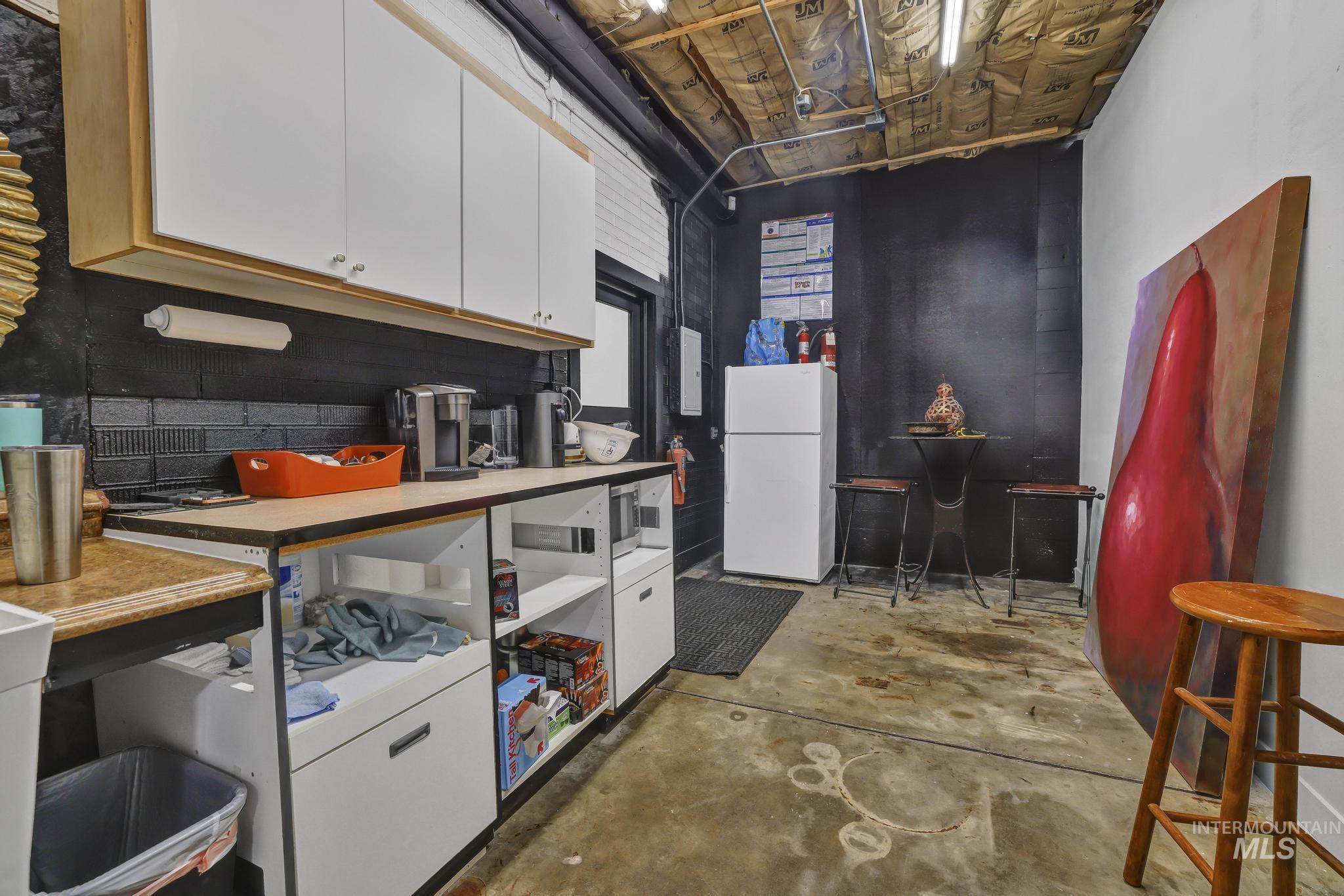 Kitchen featuring white cabinets, unfinished concrete floors, and freestanding refrigerator