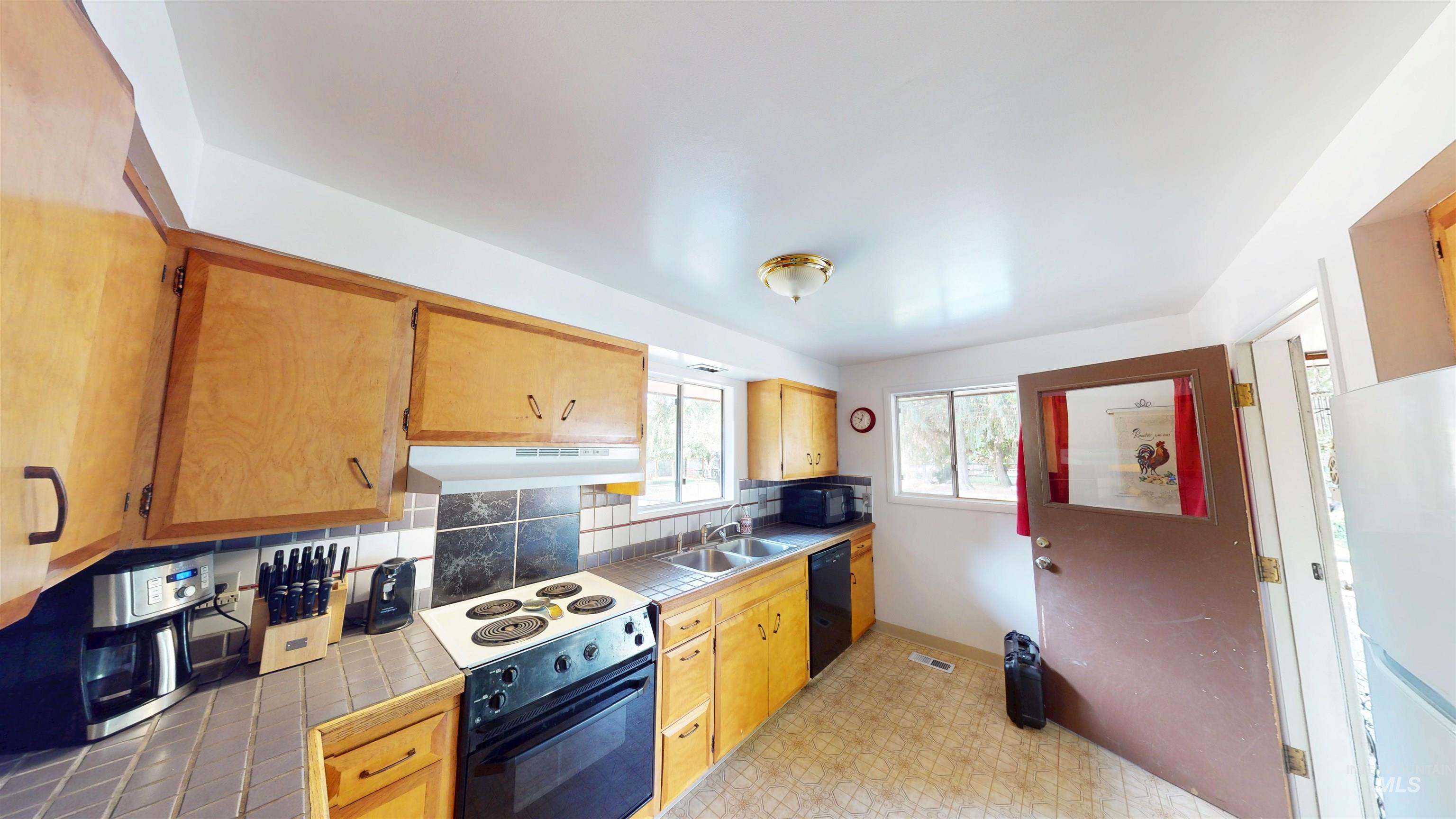 Kitchen featuring black appliances, tile counters, under cabinet range hood, tasteful backsplash, and light floors