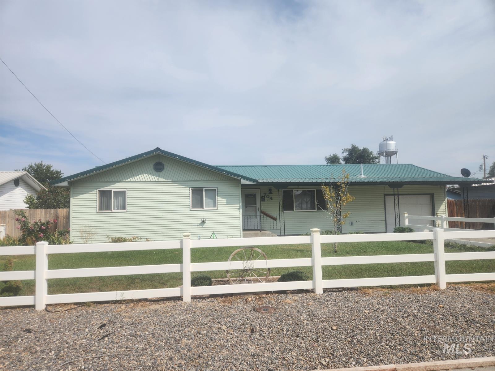 Single story home featuring a metal roof, an attached garage, a porch, a fenced front yard, and concrete driveway