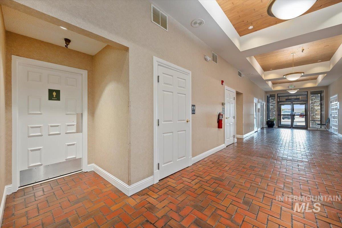 Corridor featuring a raised ceiling, brick flooring, and wooden ceiling