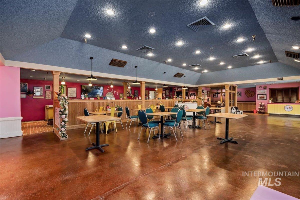Misc room with concrete flooring, a wainscoted wall, a textured ceiling, wood walls, and vaulted ceiling