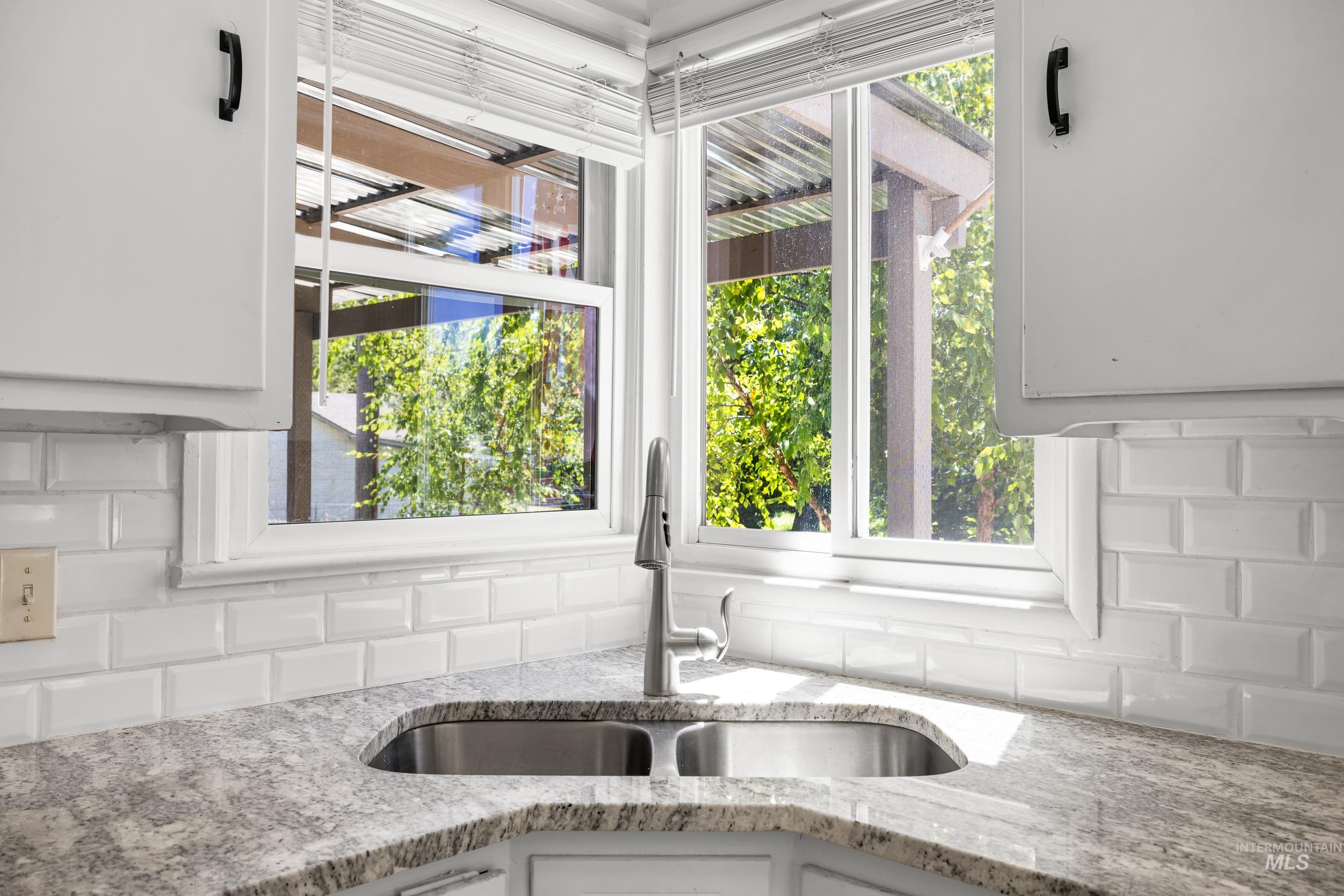 Kitchen with backsplash, light stone countertops, and white cabinets