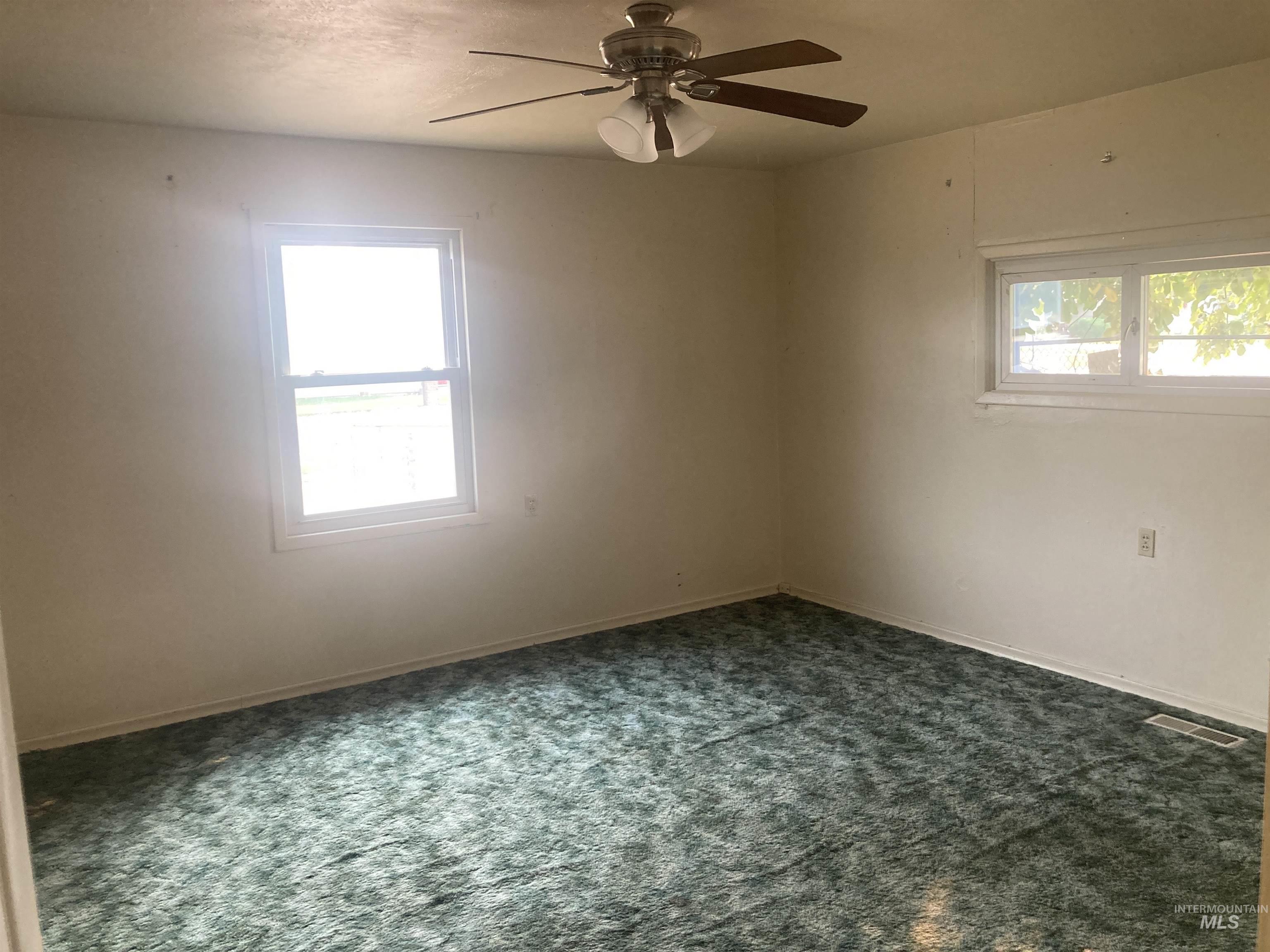 Empty room with dark colored carpet and a ceiling fan