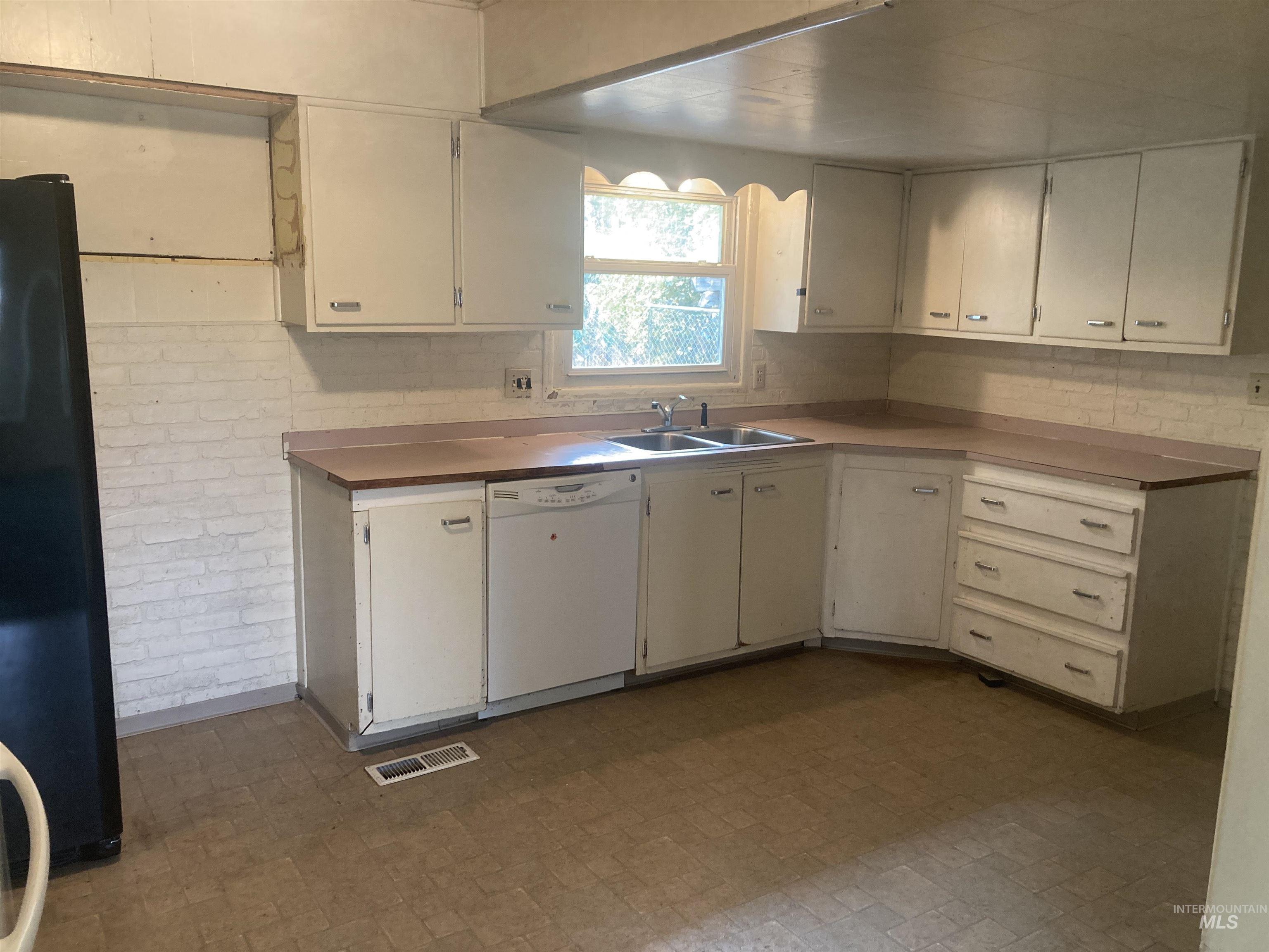 Kitchen featuring freestanding refrigerator, white dishwasher, white cabinetry, light countertops, and dark flooring