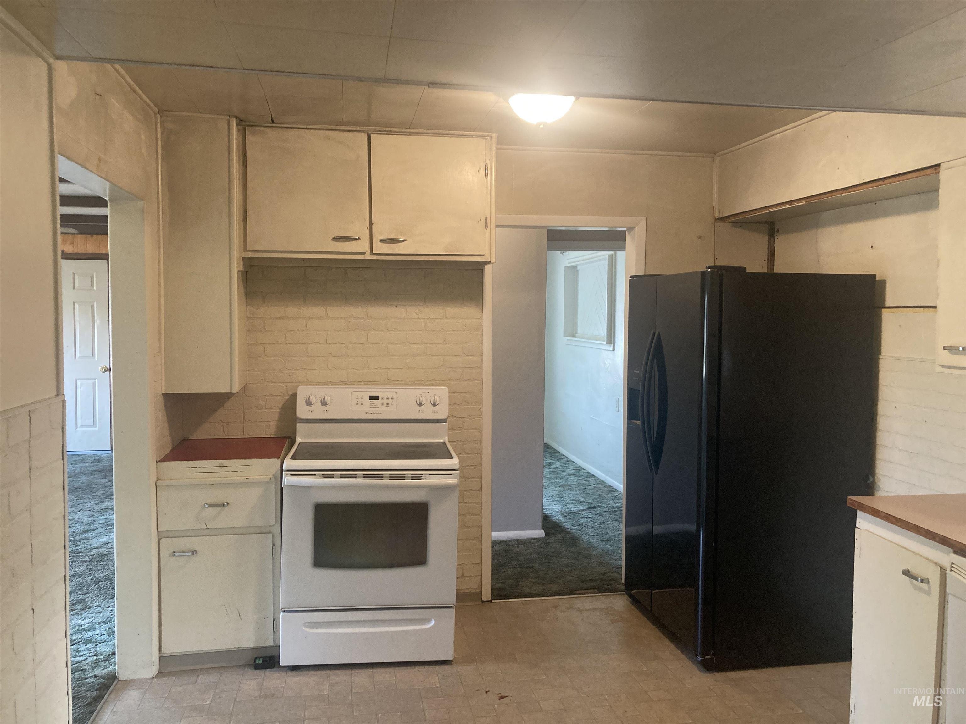 Kitchen featuring electric range, black fridge, brick wall, light countertops, and light carpet