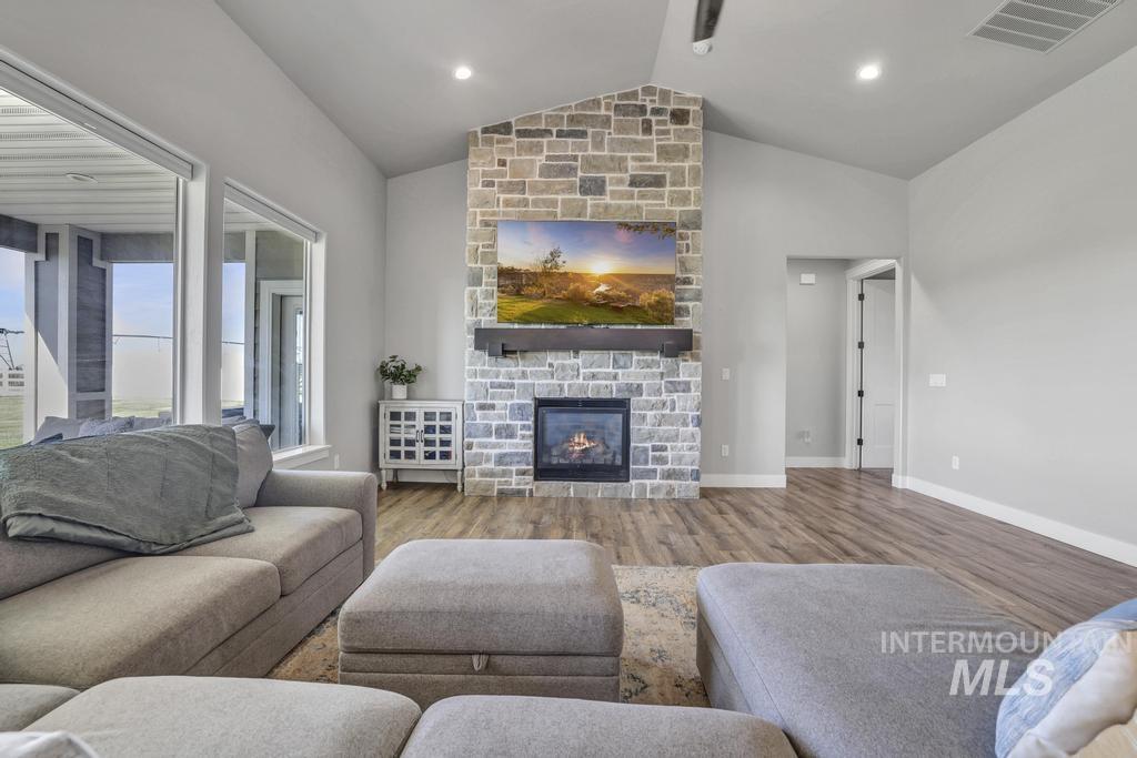 Living room featuring vaulted ceiling, a stone fireplace, and wood finished floors