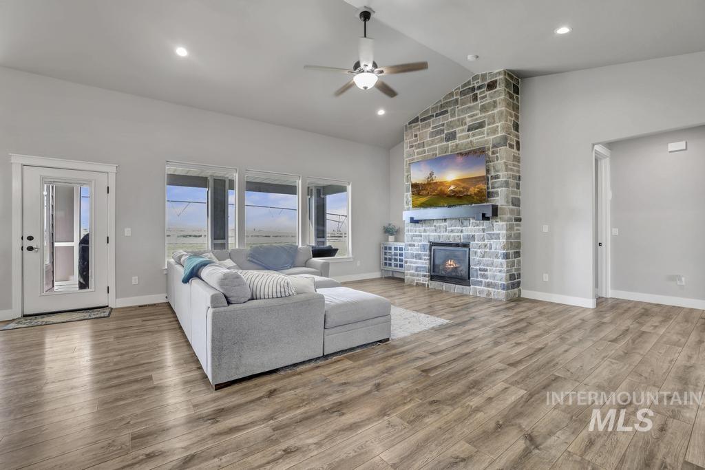 Living area featuring a stone fireplace, wood finished floors, a ceiling fan, high vaulted ceiling, and recessed lighting