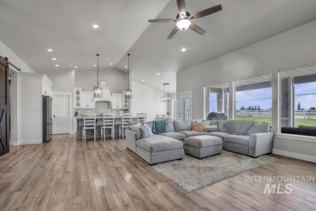 Living area with a barn door, high vaulted ceiling, a ceiling fan, light wood-style flooring, and recessed lighting