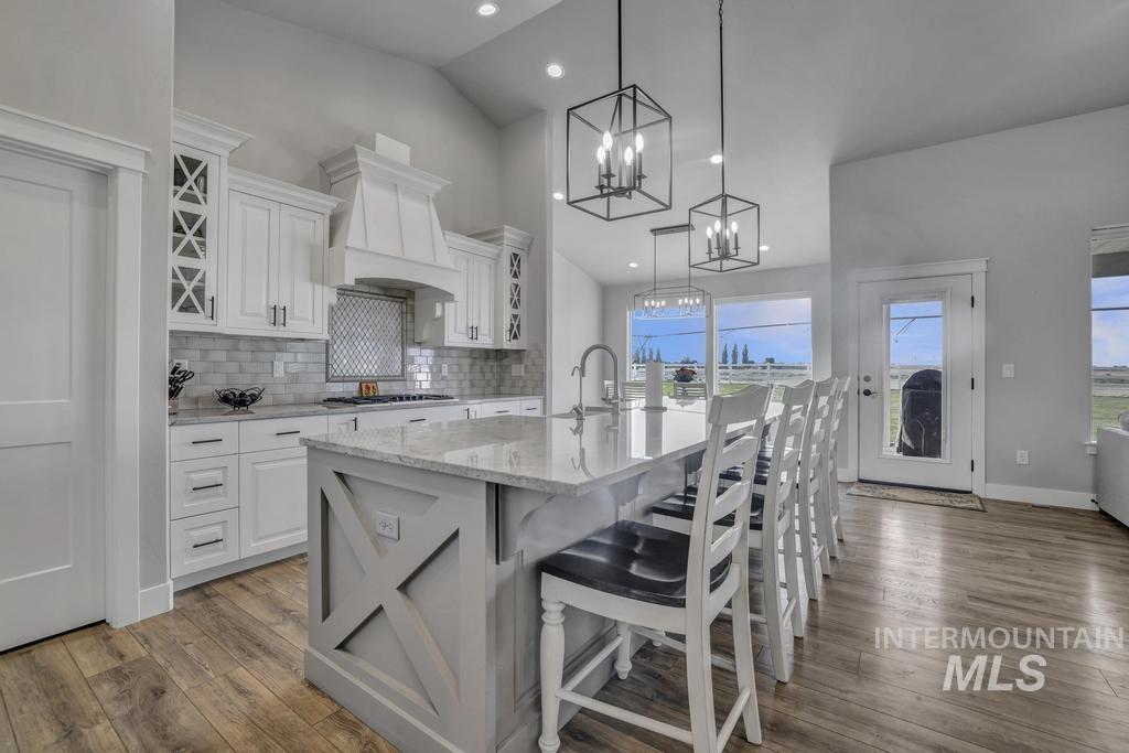 Kitchen featuring light stone counters, a breakfast bar, a center island with sink, backsplash, and white cabinetry