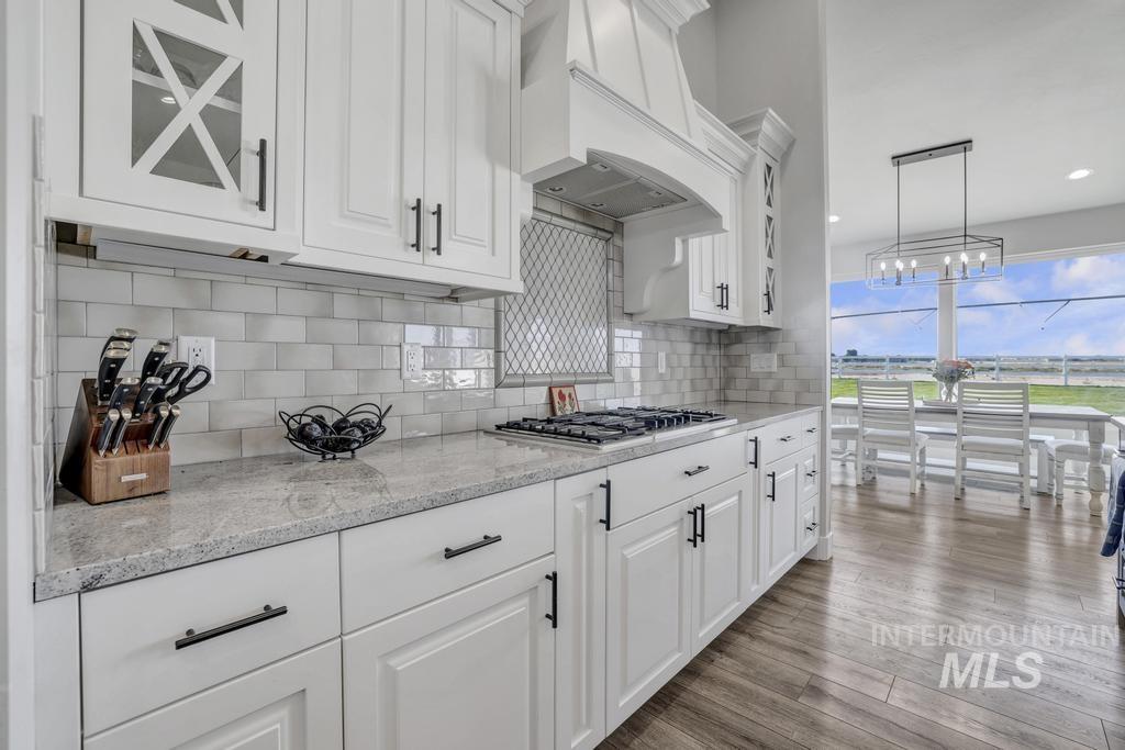 Kitchen with white cabinets, backsplash, light stone countertops, light wood-style floors, and decorative light fixtures