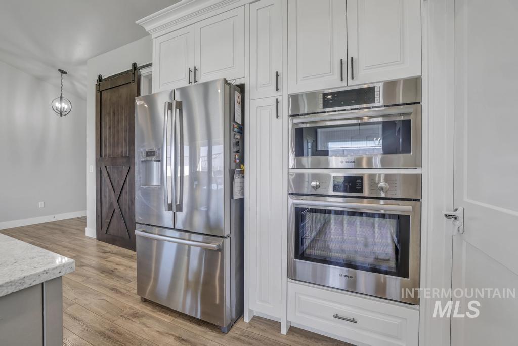 Kitchen featuring a barn door, appliances with stainless steel finishes, light wood-style flooring, pendant lighting, and white cabinetry