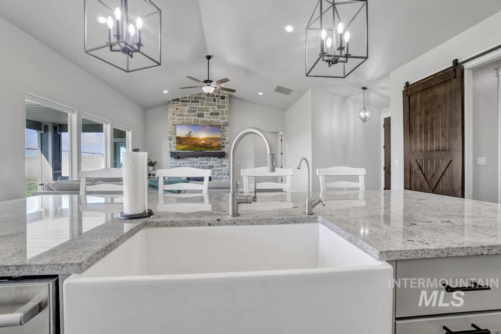 Kitchen with a chandelier, lofted ceiling, light stone counters, ceiling fan, and a barn door