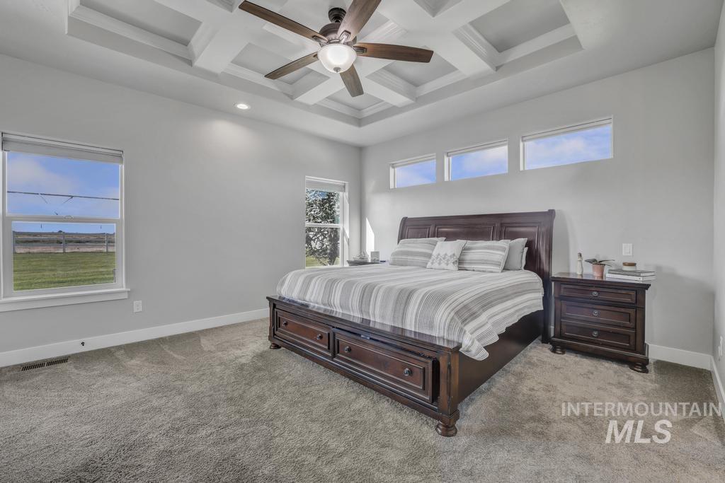 Bedroom featuring beamed ceiling, coffered ceiling, light carpet, and ceiling fan