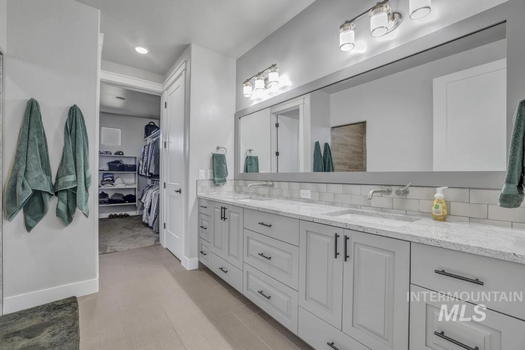 Full bath with double vanity, a spacious closet, recessed lighting, and backsplash