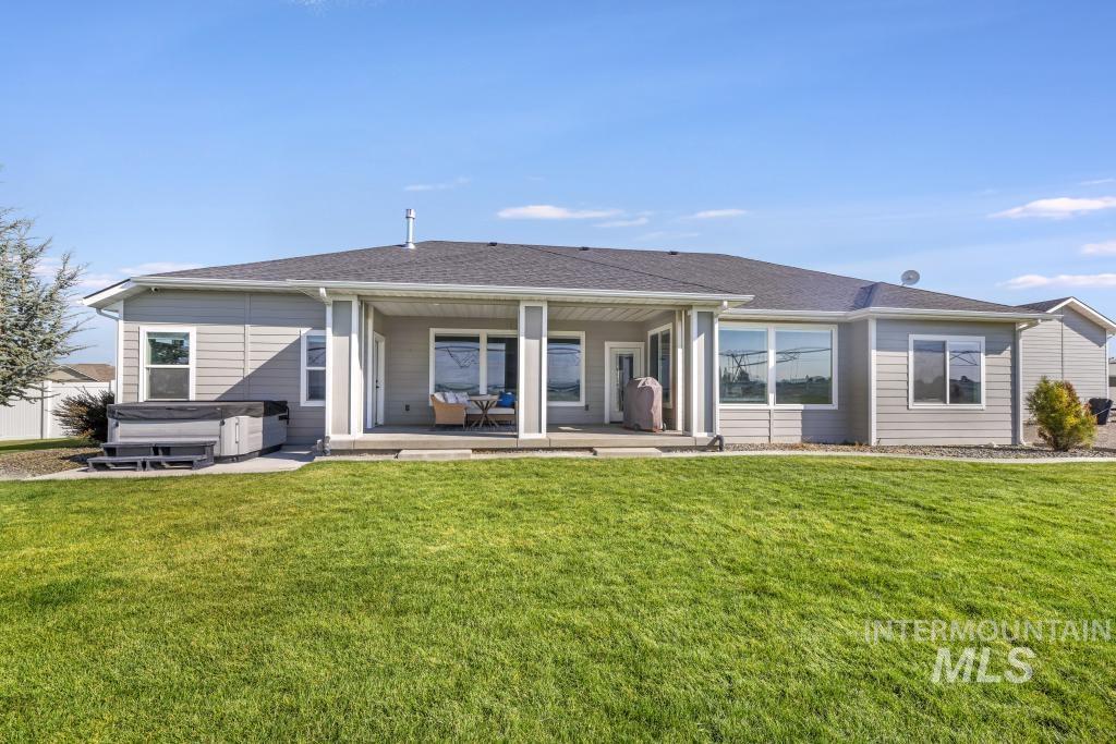 Rear view of house with a hot tub, a patio, roof with shingles, and a lawn