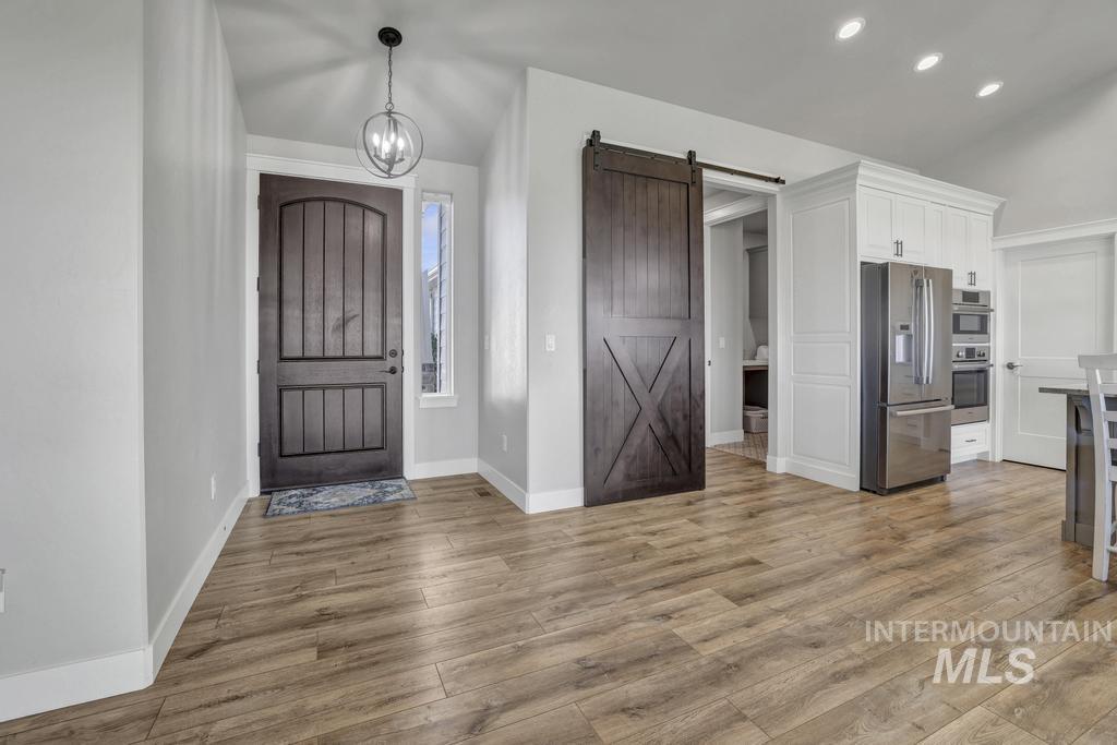 Foyer entrance with recessed lighting, light wood-type flooring, a barn door, and a chandelier