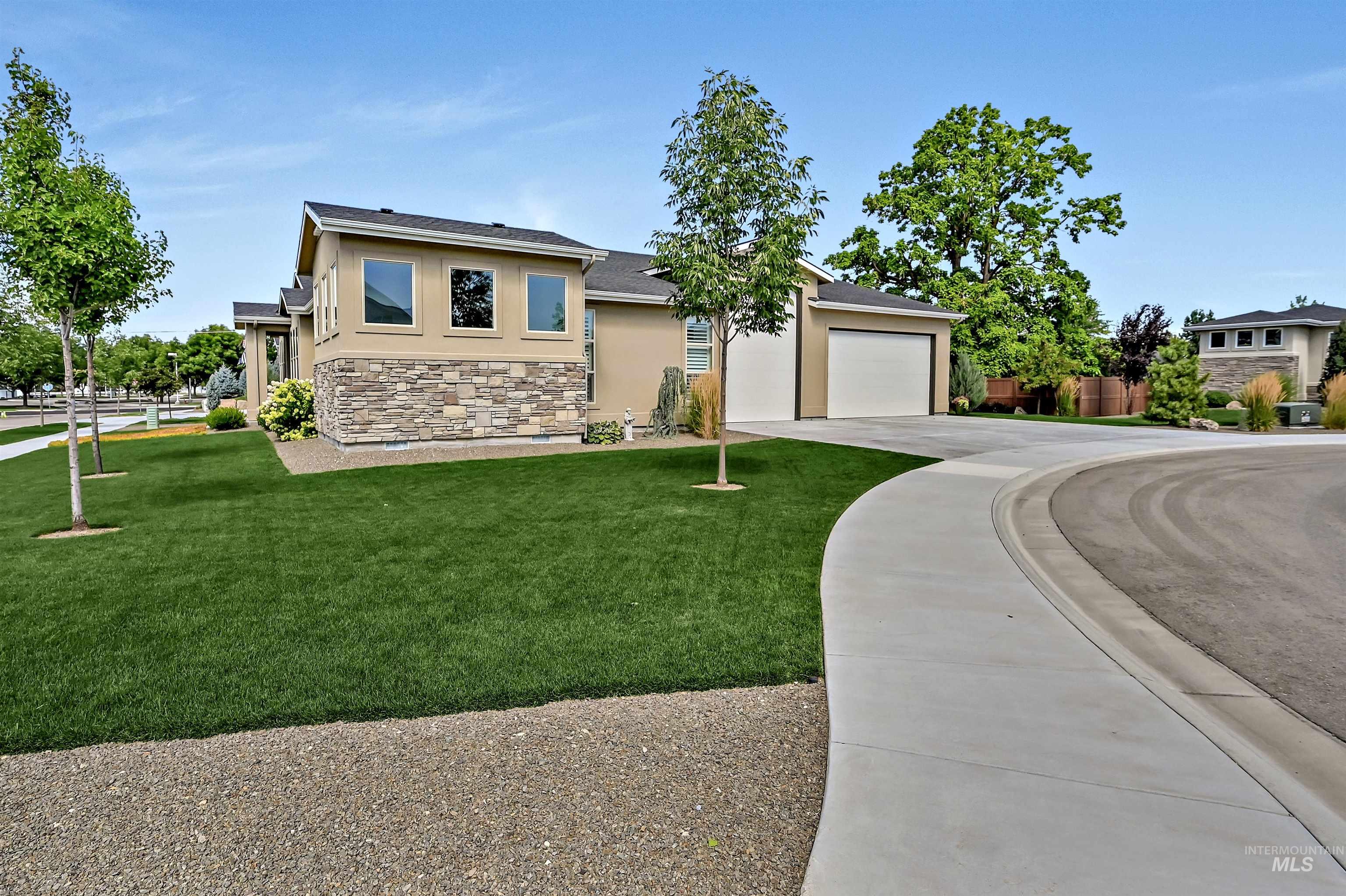 Stucco siding, concrete driveway, stone siding, and a front lawn