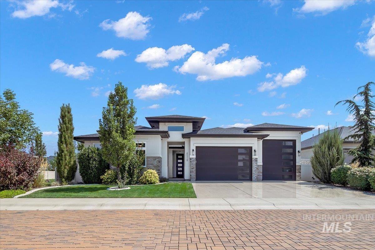 Prairie-style house with a garage, concrete driveway, stucco siding, stone siding, and a front yard