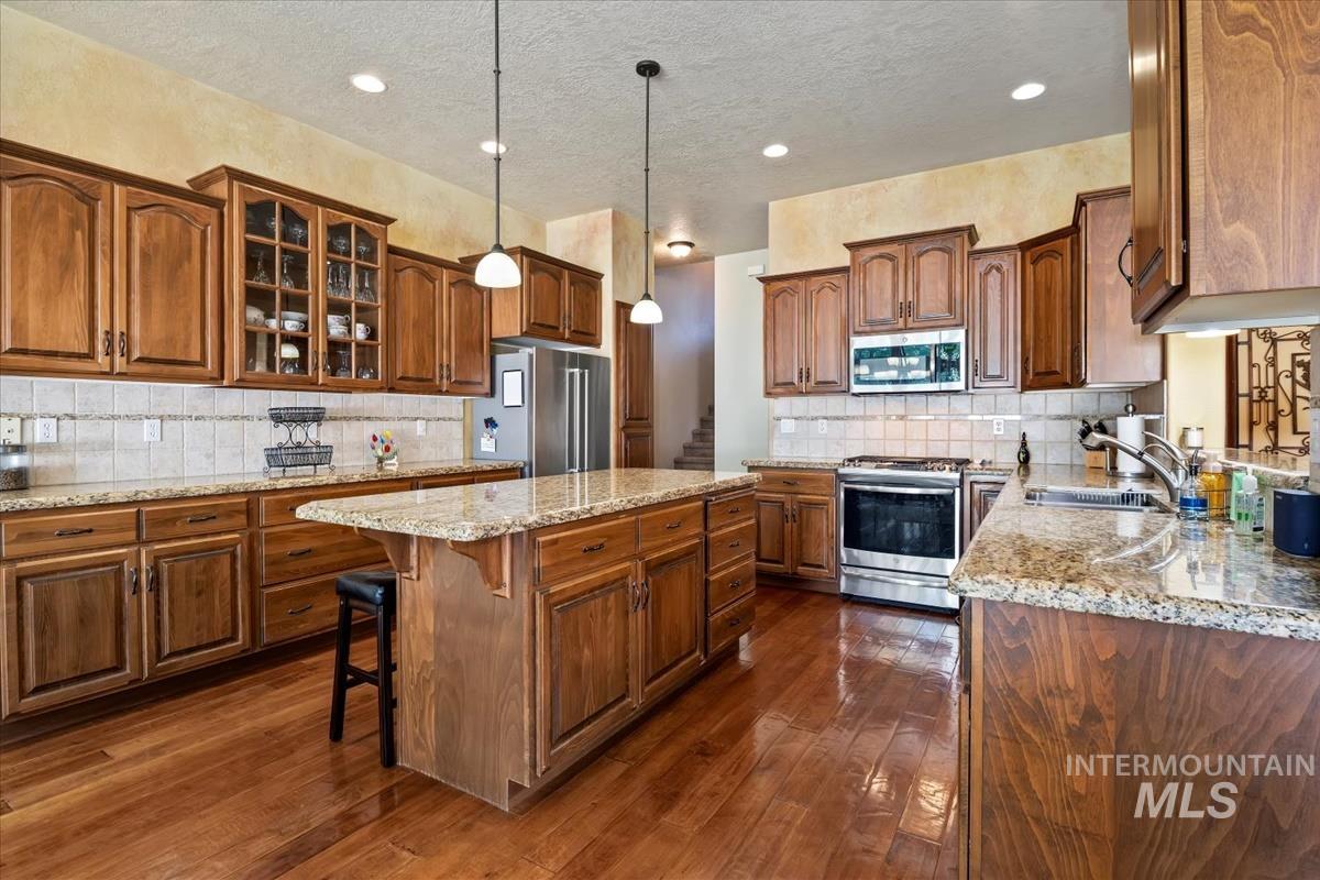 Kitchen with glass insert cabinets, light stone countertops, stainless steel appliances, decorative backsplash, and a breakfast bar